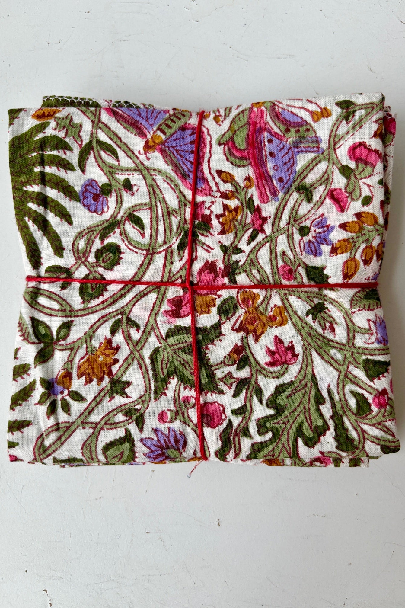 Set of four hand sewn fabric napkins with green and pink floral butterfly and palm motif on a white background on a white table
