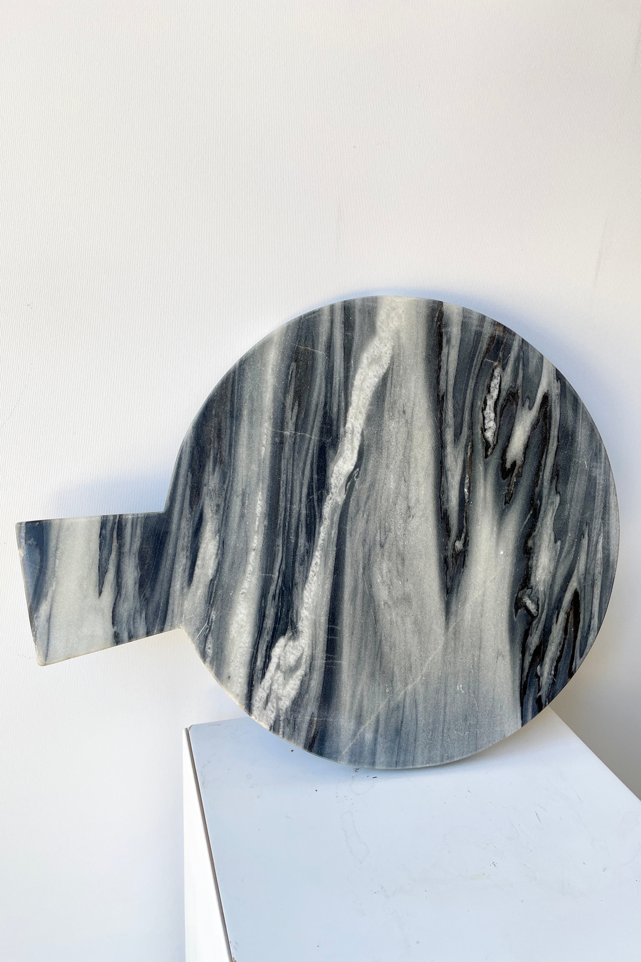 The black marble cheese board at Sprout Home leaning on its side against a white wall.