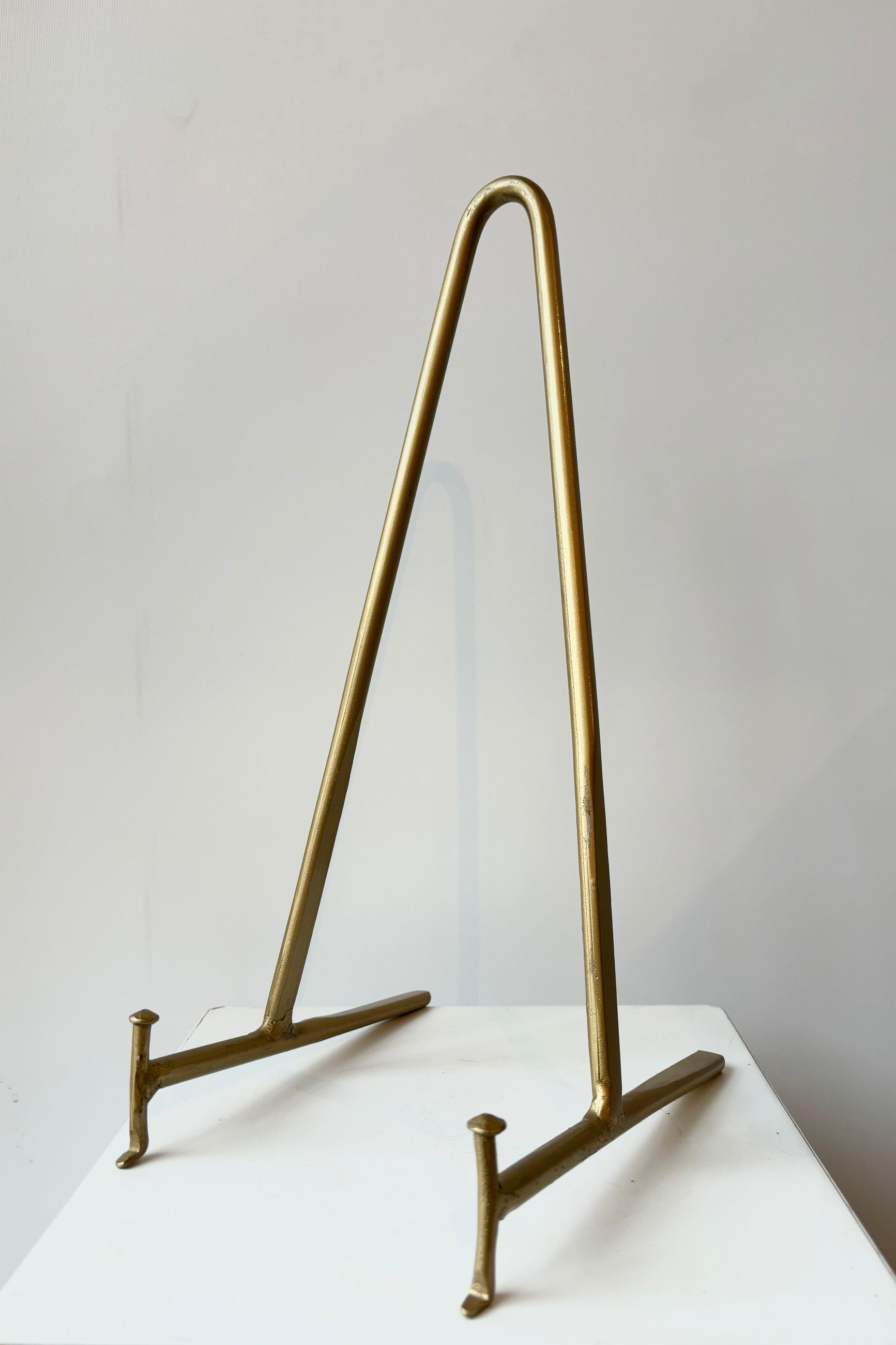 Brass display stand featuring two horizontal prongs connected by a vertical arch for support against a white background ©Sprout Home
