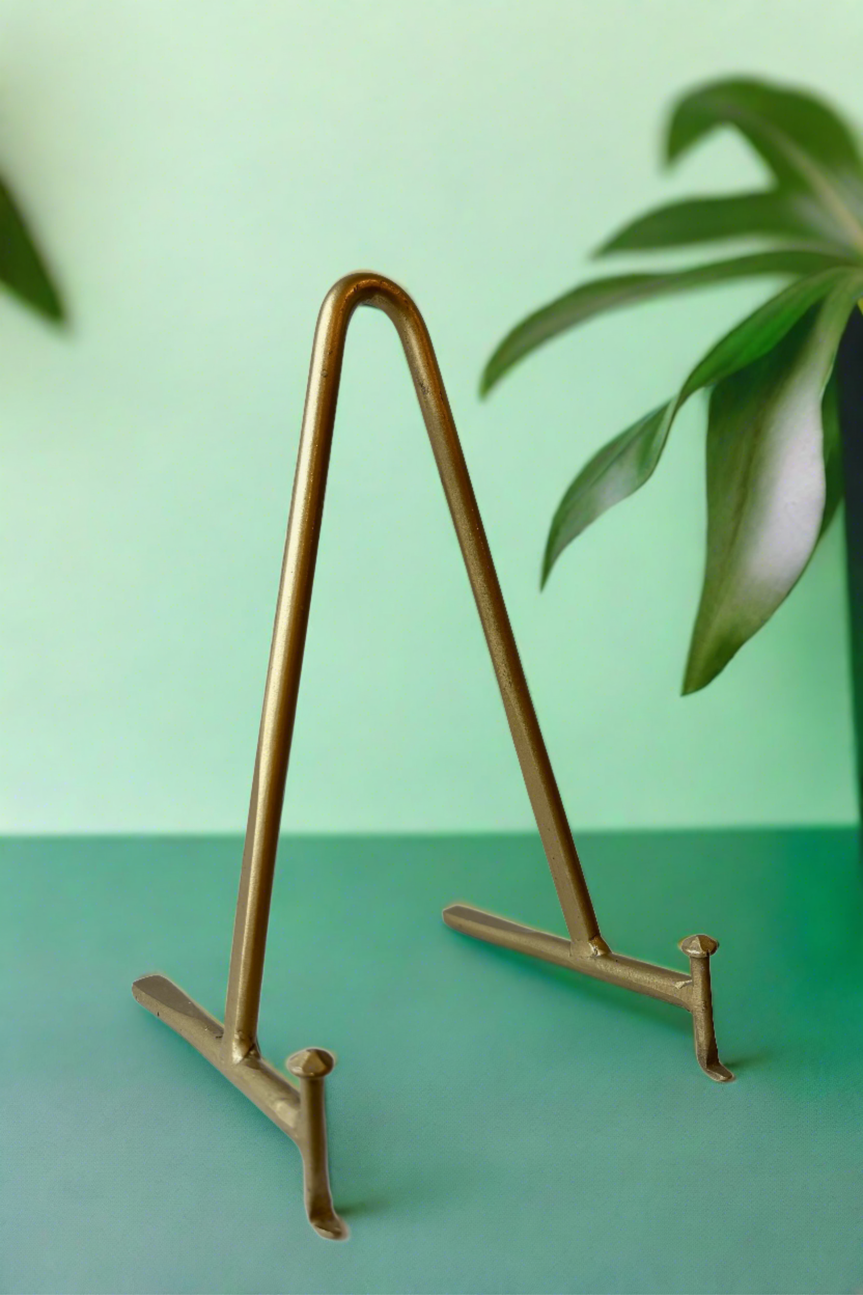 A gold colored display stand sitting on a green surface with leaves in the background ©Sprout Home