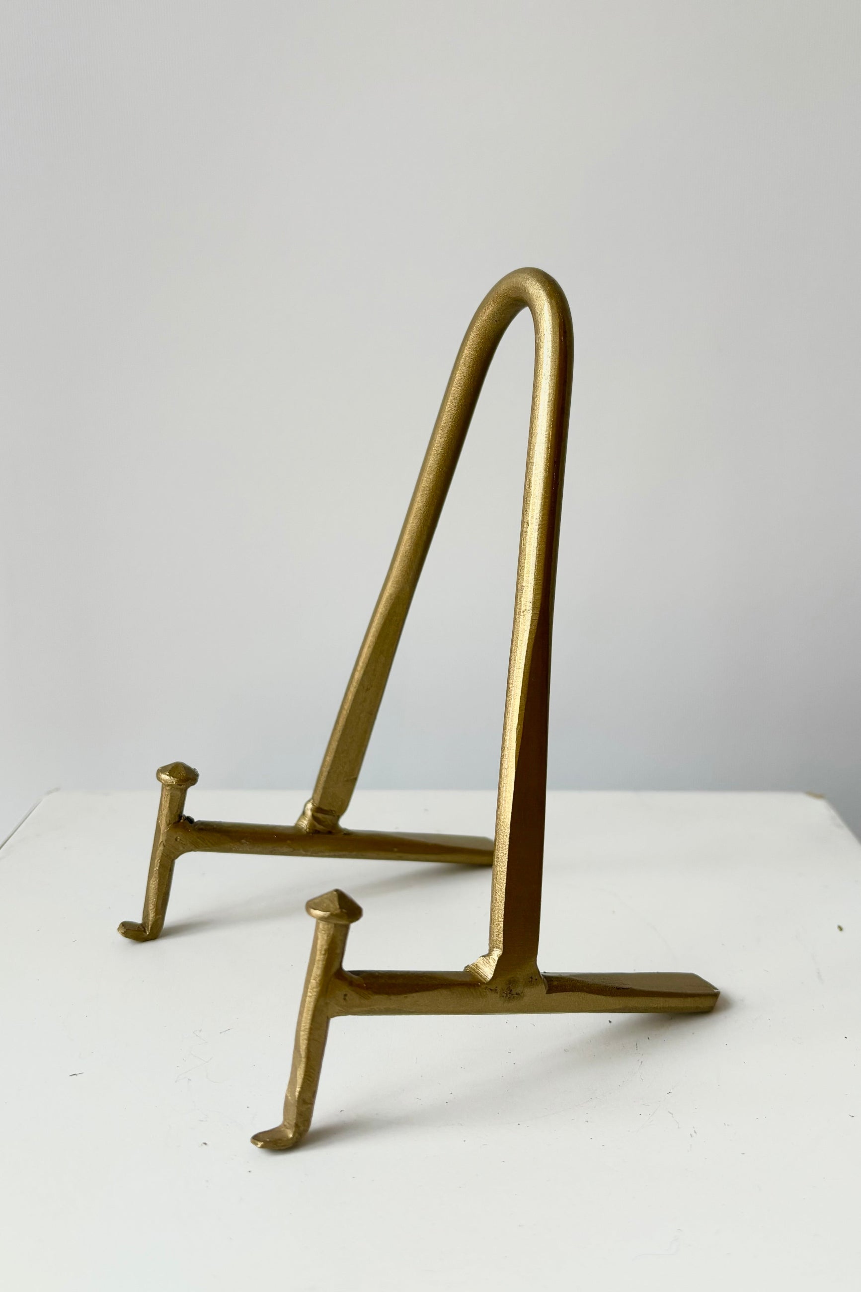 Brass display stand featuring two horizontal prongs connected by a vertical arch for support against a white background ©Sprout Home