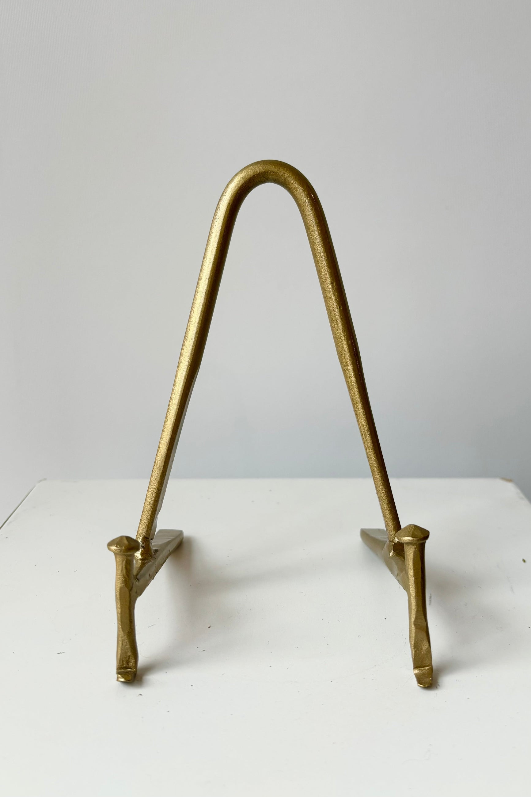 Front view of brass display stand featuring two horizontal prongs connected by a vertical arch for support against a white background ©Sprout Home