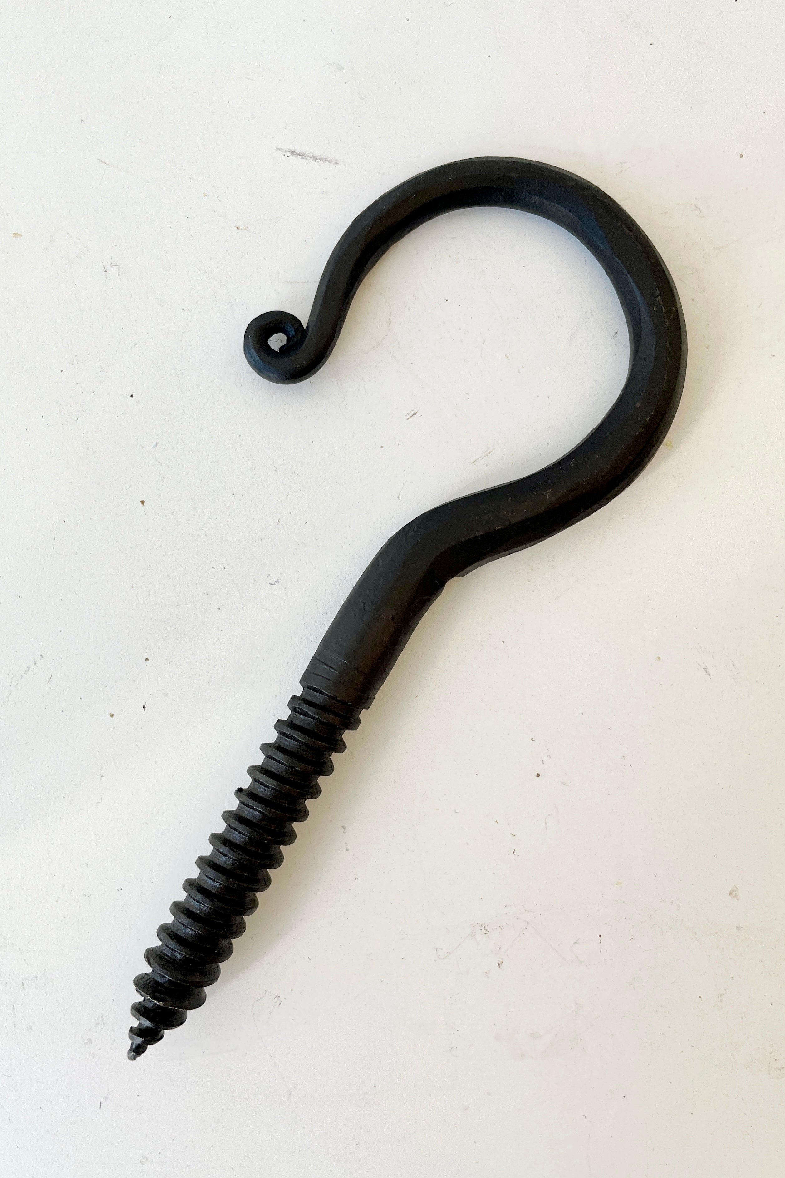 A threaded blacksmiths hook at Sprout Home against a white wall.