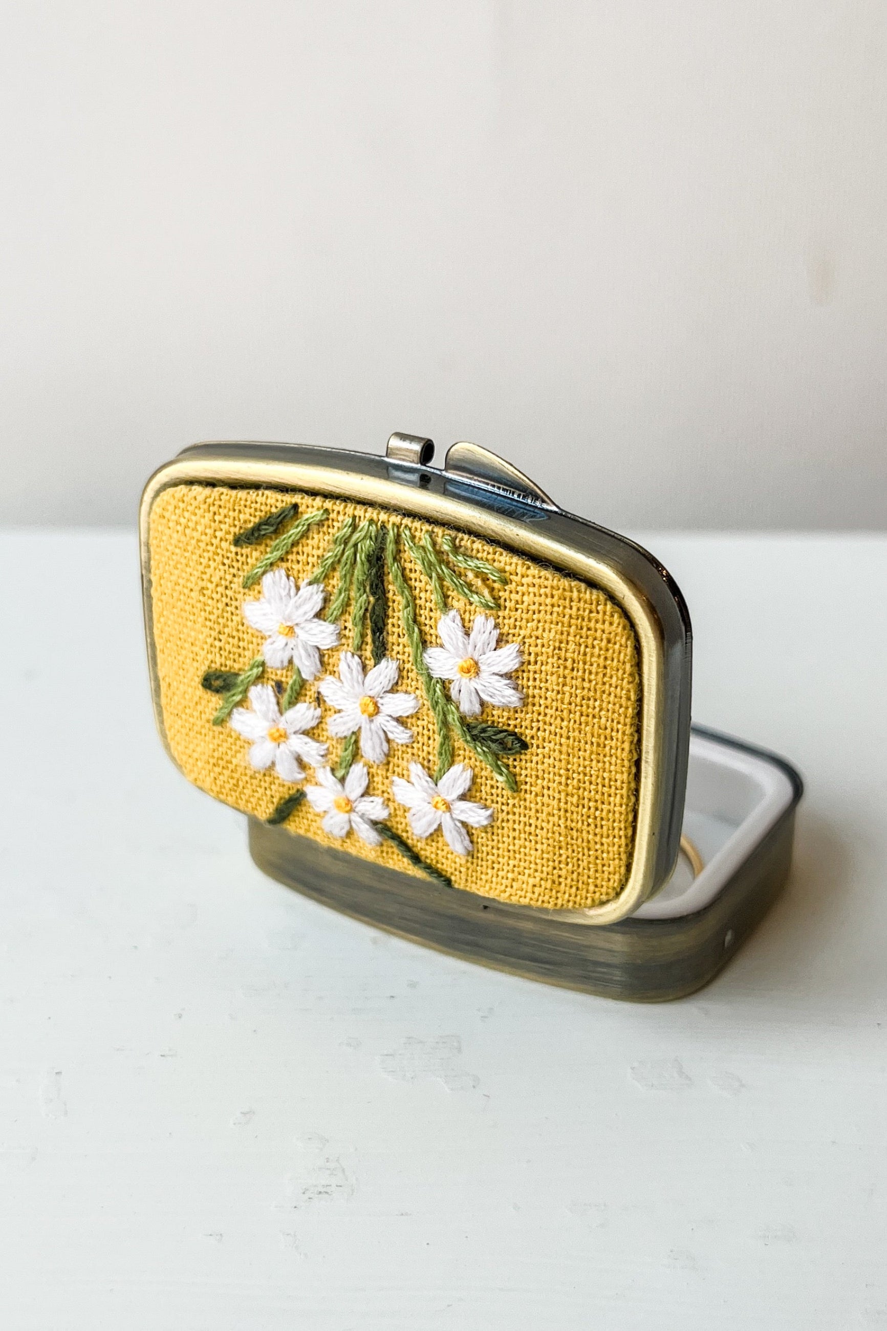 Small rectangular mirror with floral embroidery on a white surface ©Sprout Home