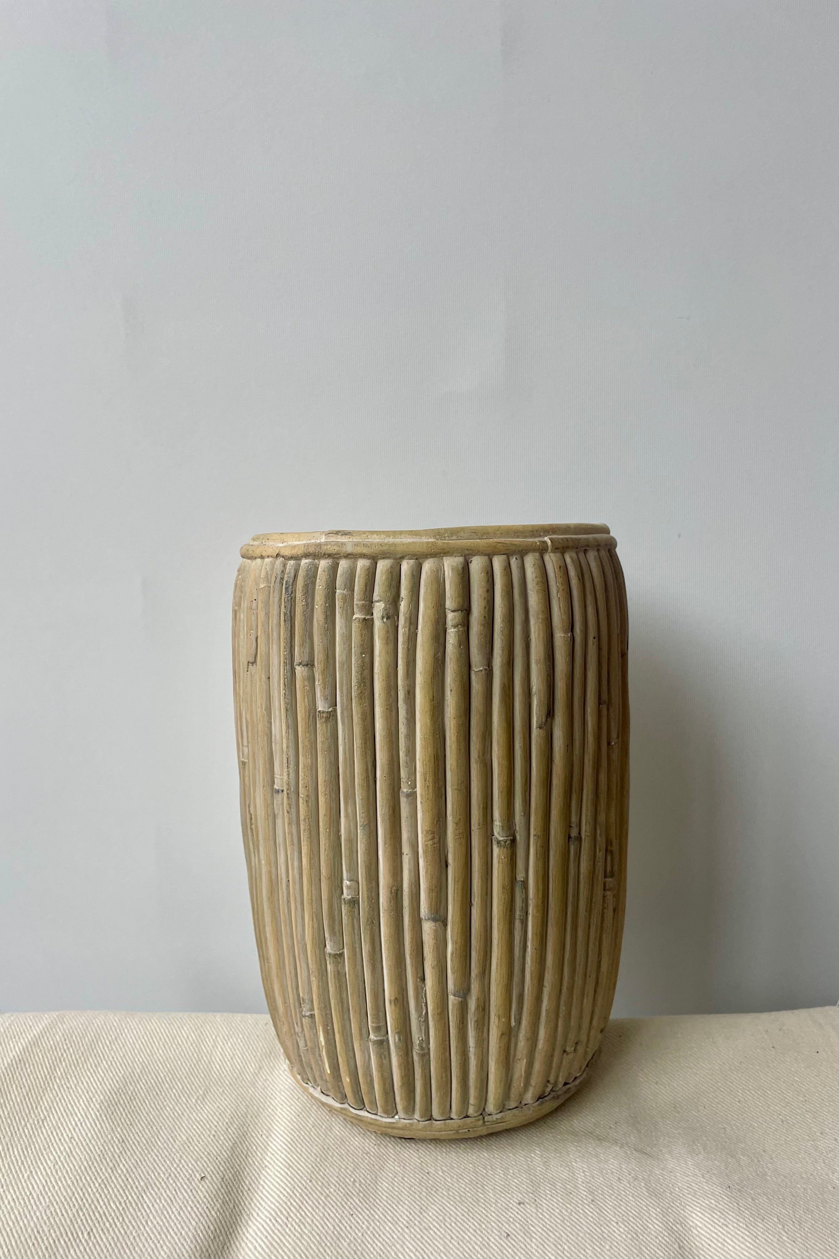 Medium tall concrete faux rattan planter against a white wall on a white tablecloth shown from the side.