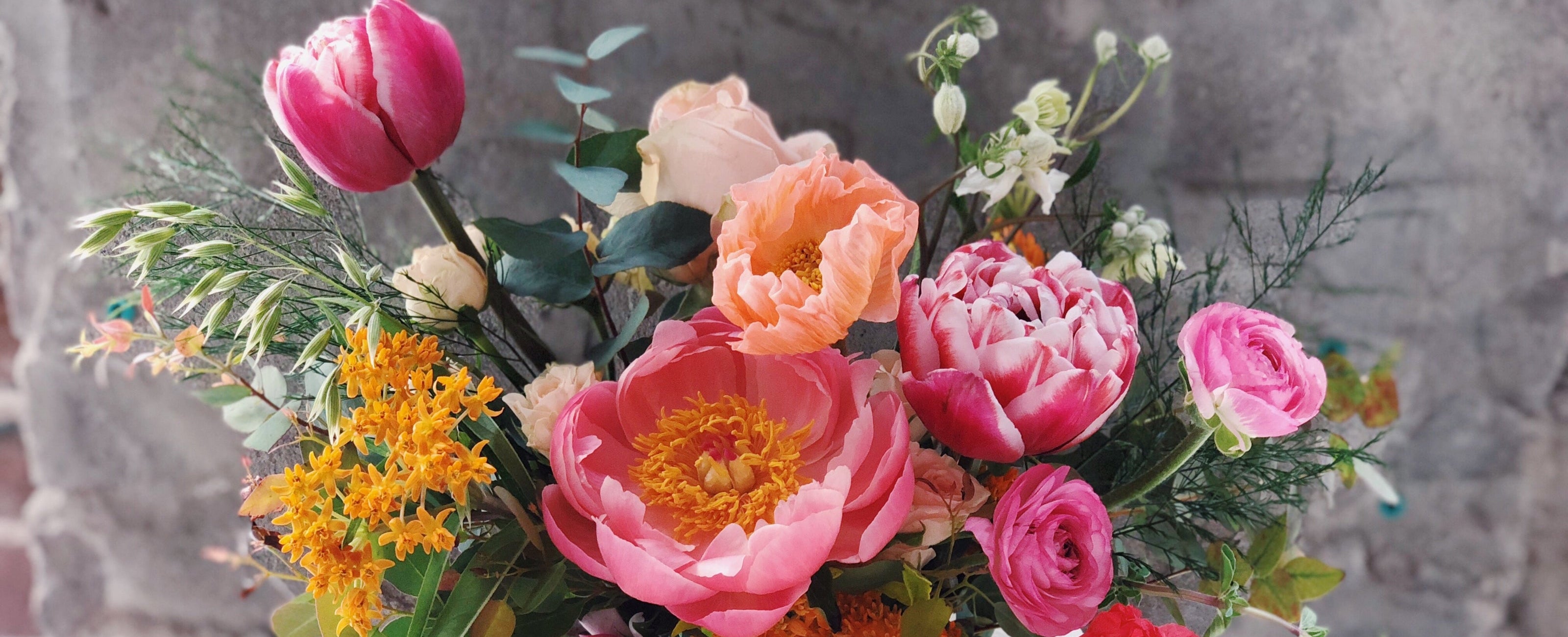 Bouquet of colorful flowers in a clear vase against a gray stone wall ©Sprout Home