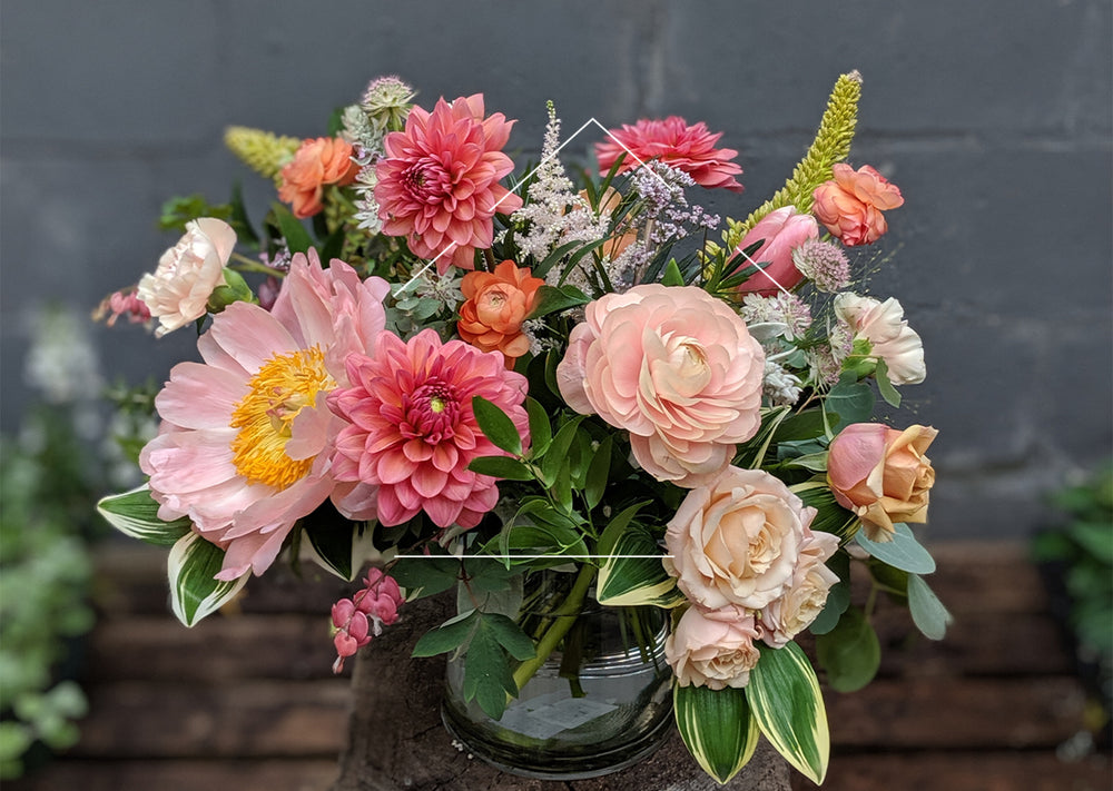 Floral arrangement featuring pink and peach flowers against a grey wall
