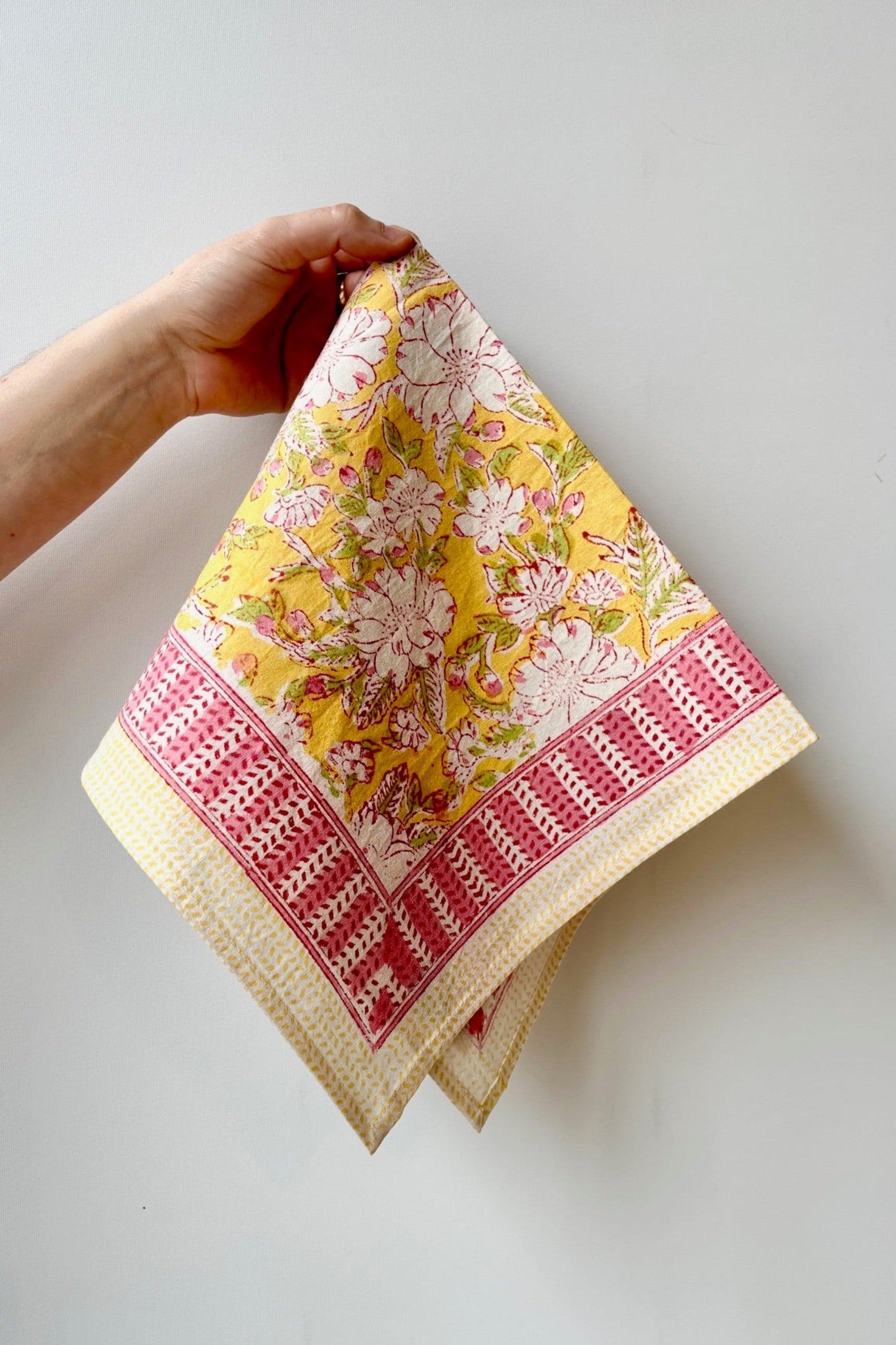 Hand printed, 100%cotton, Camelia yellow and pink floral print napkin against a white wall ©Sprout Home