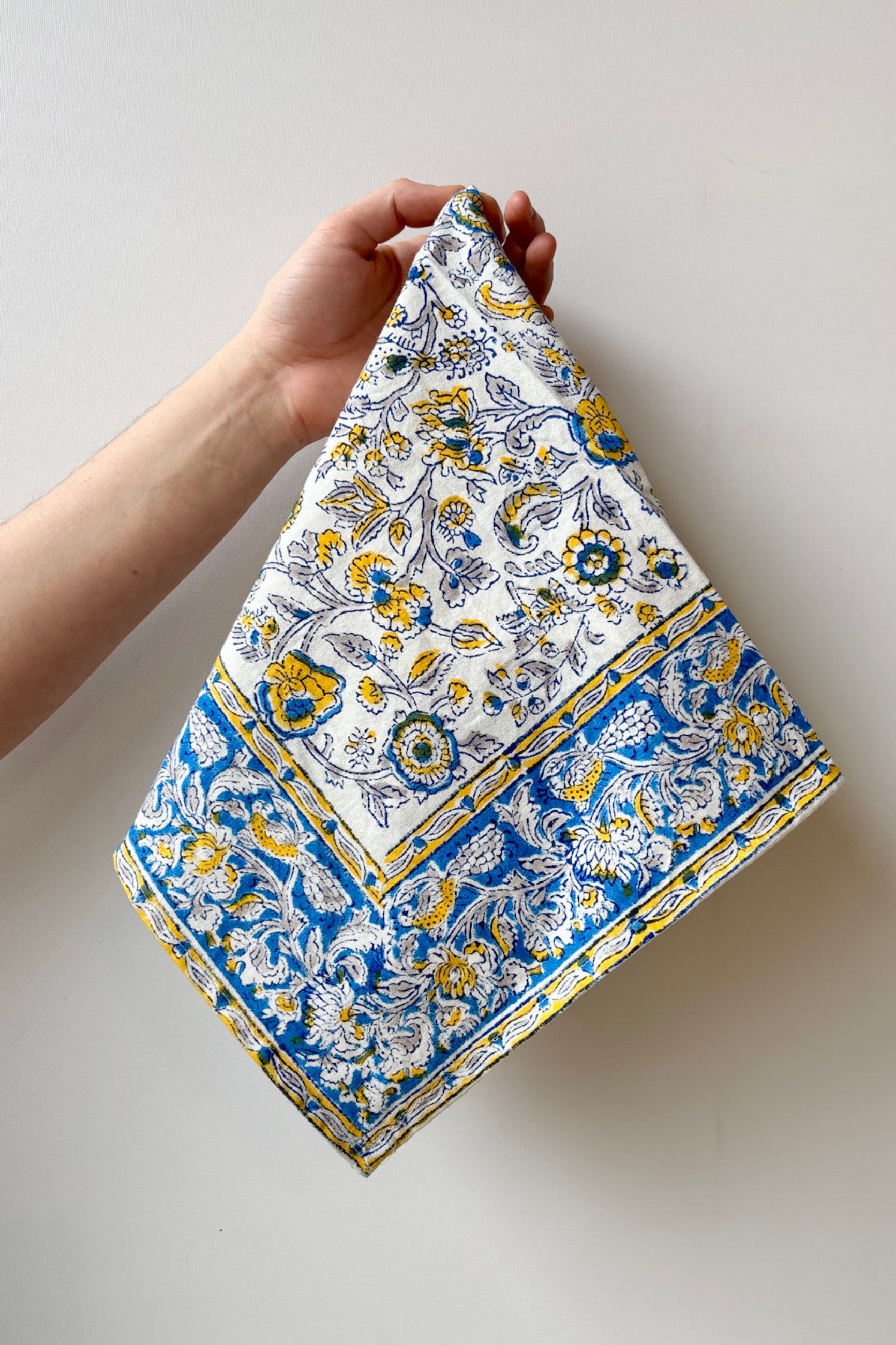 Hand printed, 100% cotton, Provence napkin with yellow and blue floral pattern against a white wall ©Sprout Home