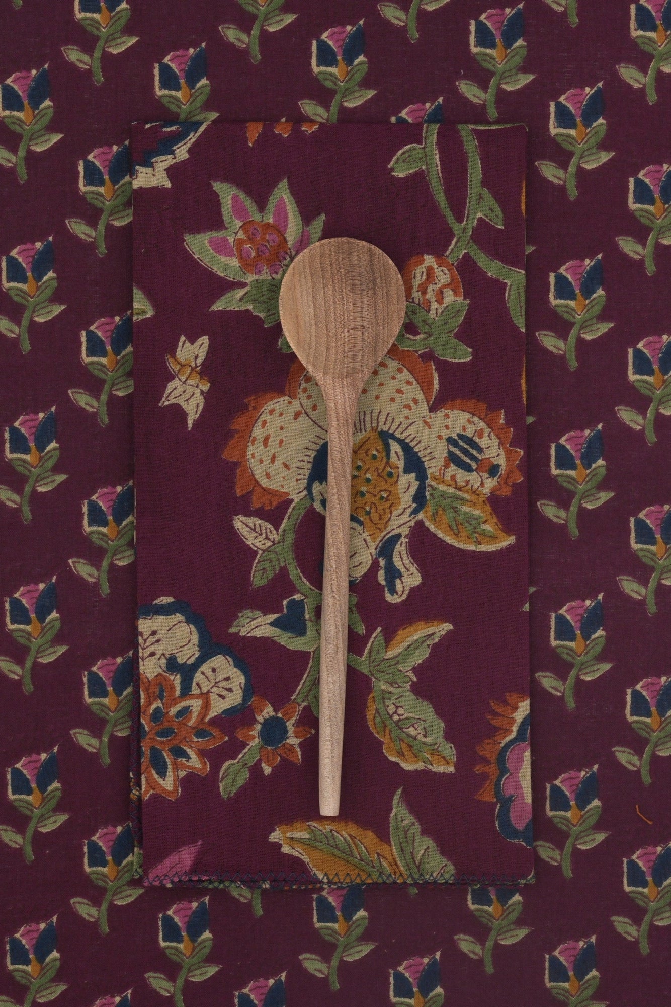 A wooden spoon on a floral patterned linen with a plum background  ©Suzette a Table
