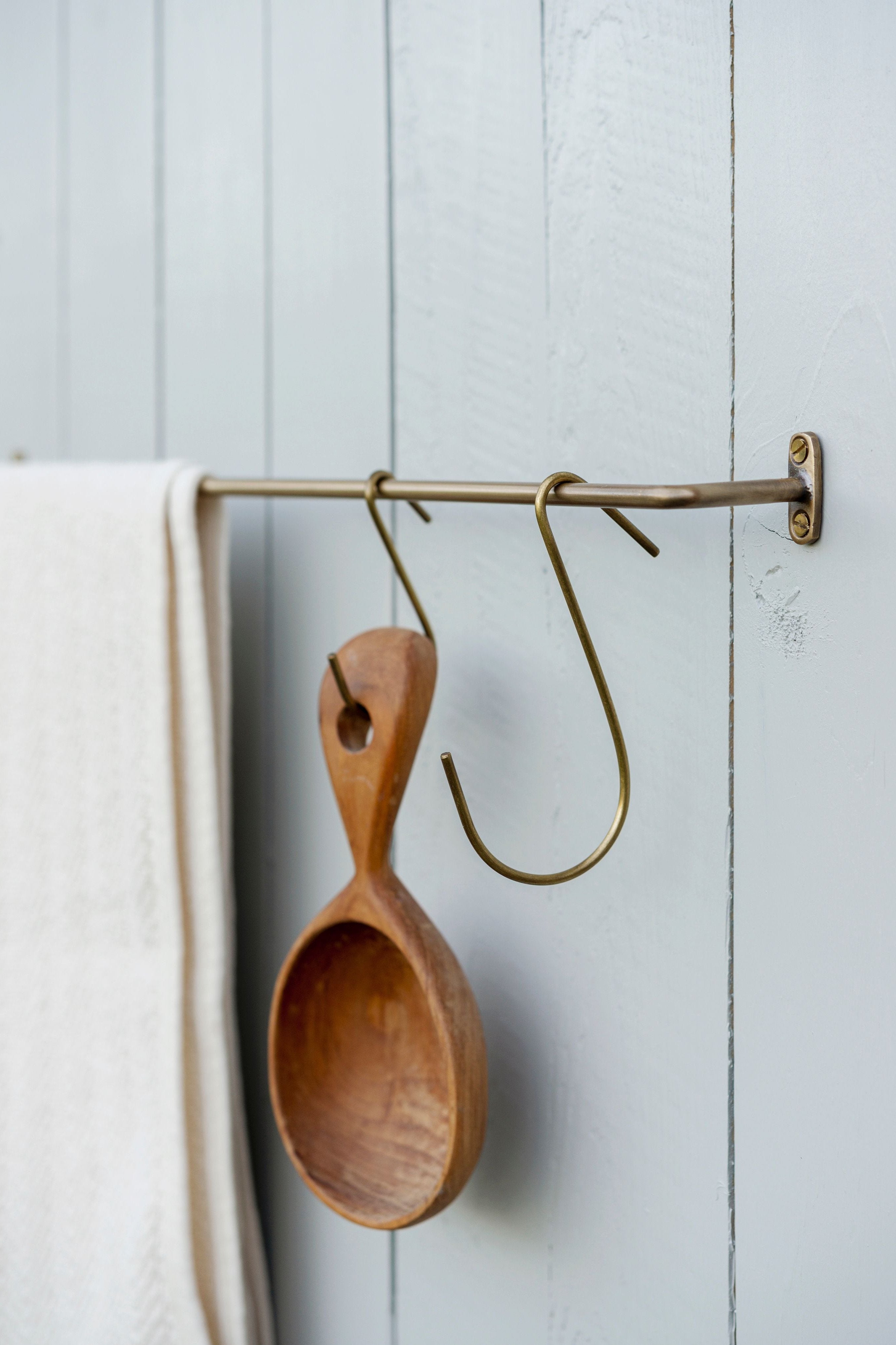 Brass hooks by Fog Linen Work hangin from a bar with a towel .