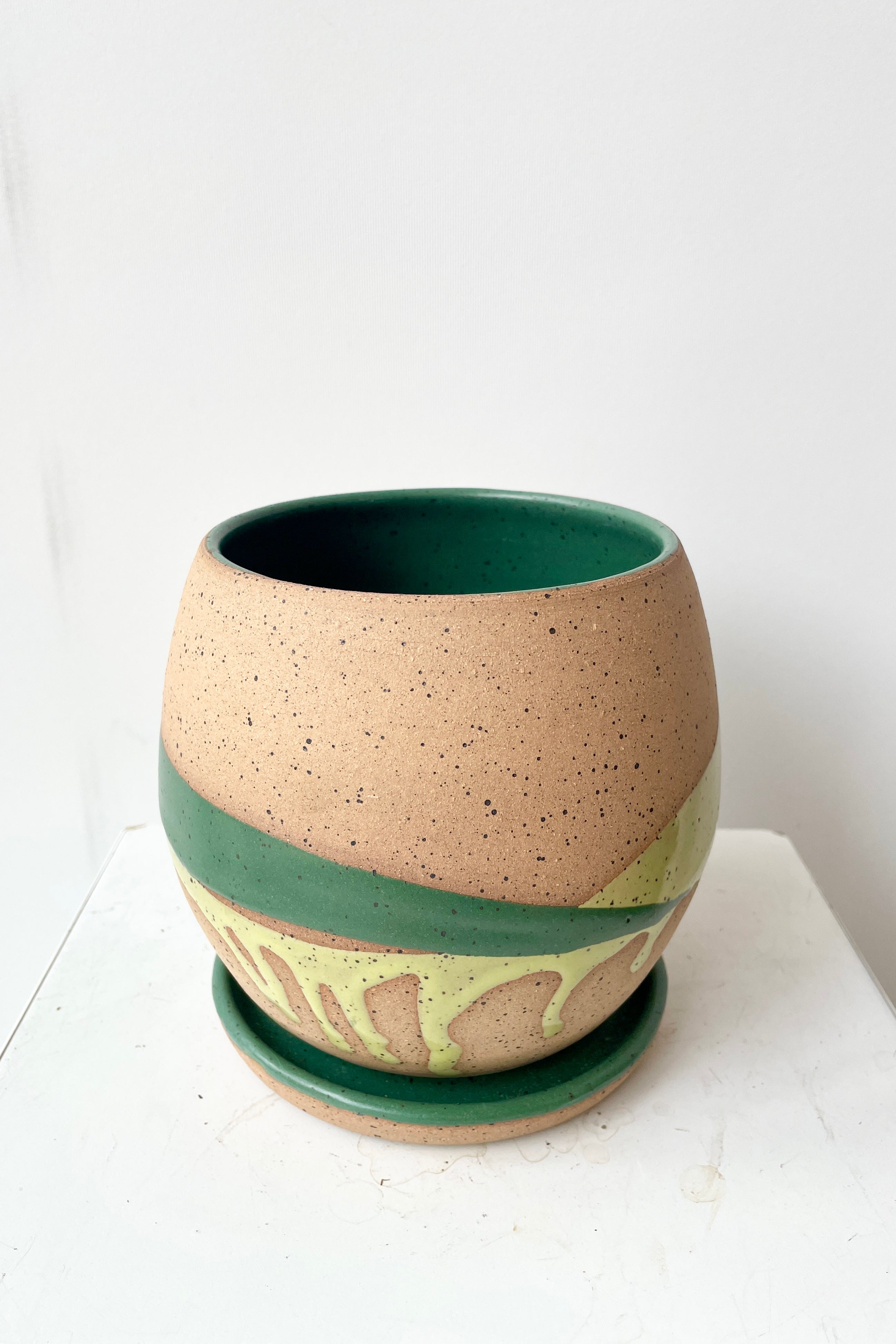 Orb Pot and saucer in Green Splash shown empty against a white wall looking in from the side.