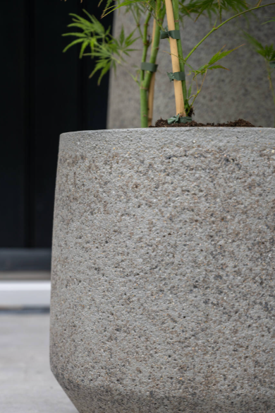 A close photo of a textured gray pot with a taper at the base. Shown in a dark room. ©Sprout Home