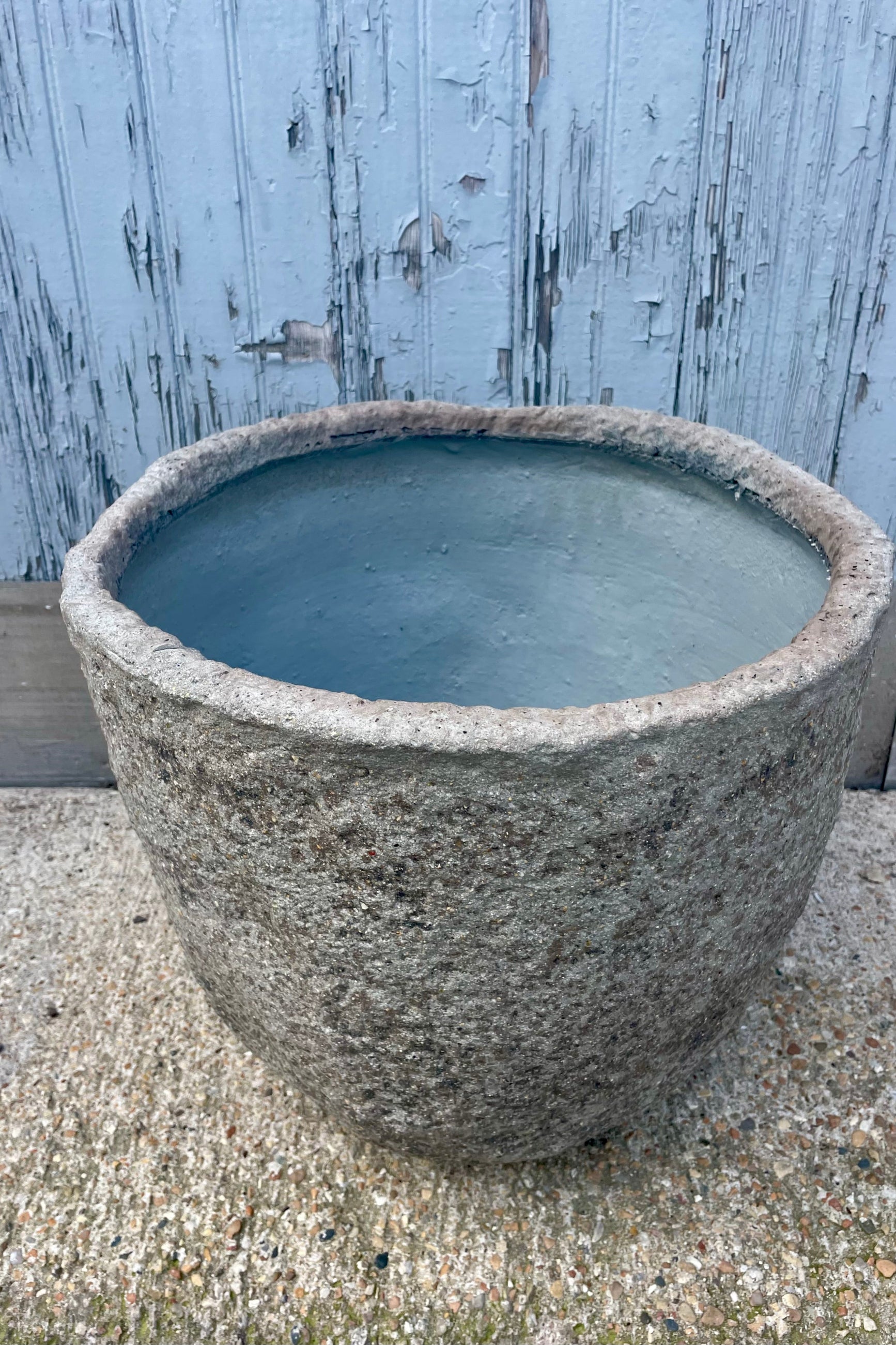 Close photo showing the side and interior opening of a textured gray pot in front of a wooden wall ©Sprout Home