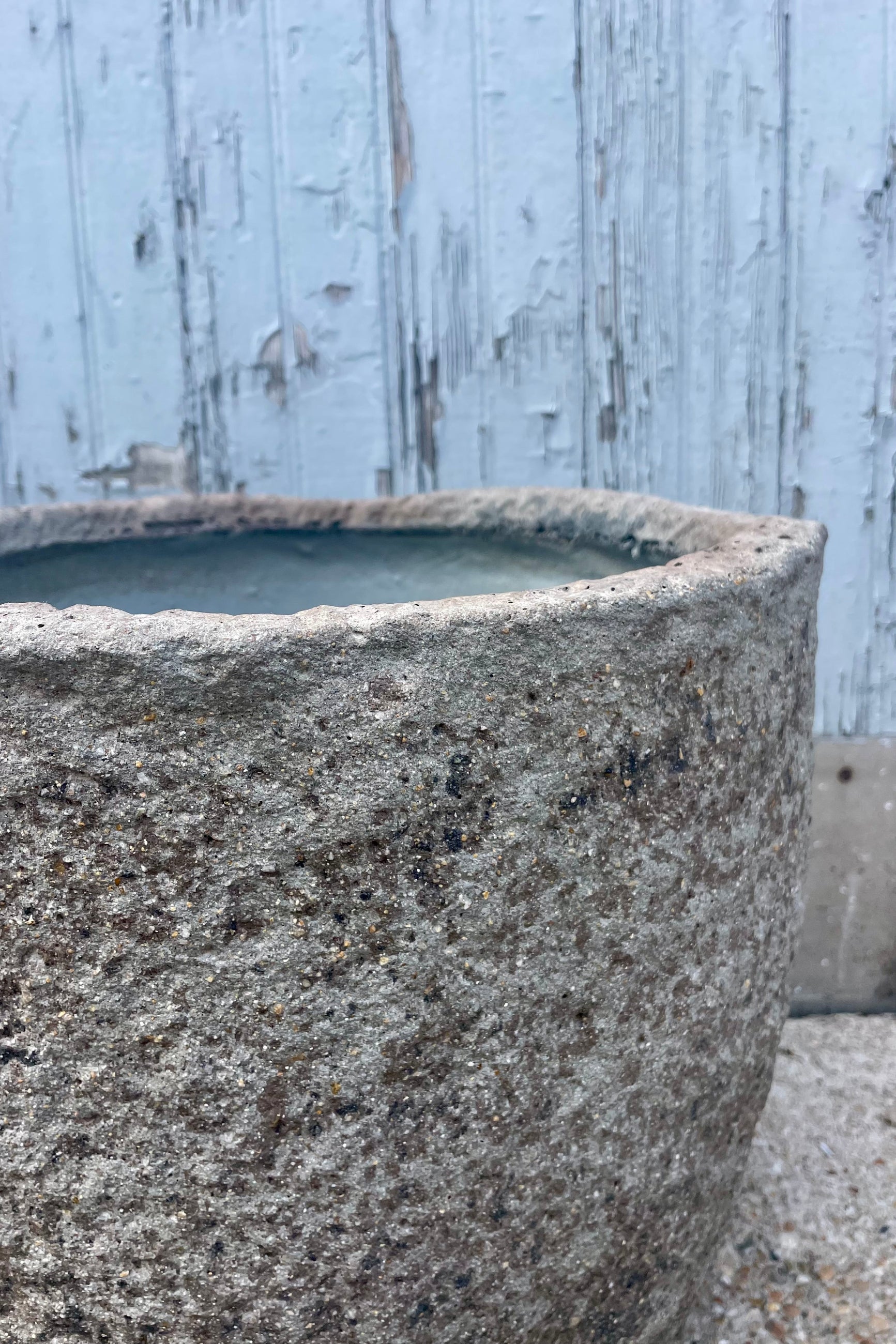 Close photo showing the side and interior opening of a textured gray pot in front of a wooden wall ©Sprout Home