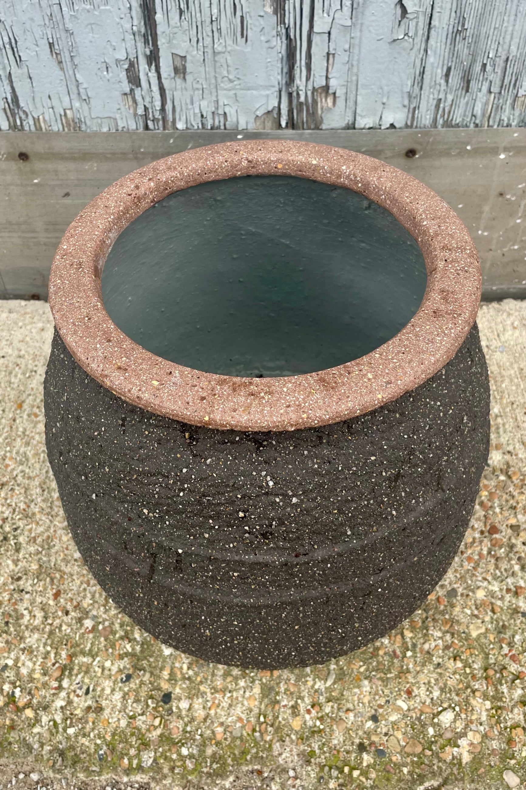 A brown clay pot with a central textural band in front of a wooden wall. Show from the above ©Sprout Home