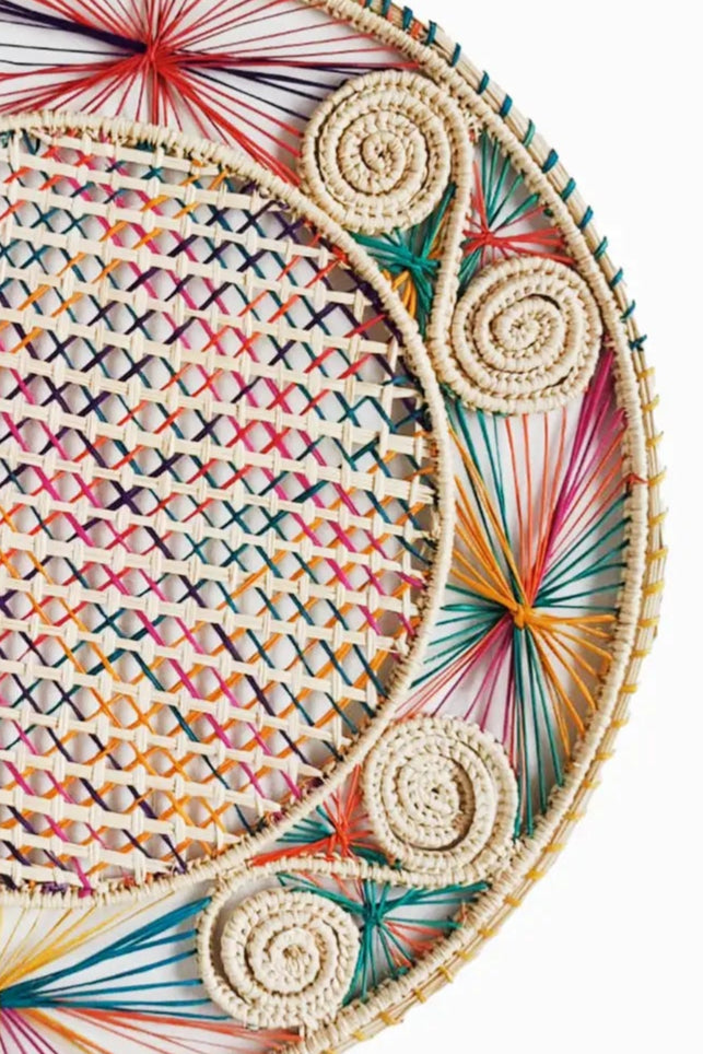 Photo of a natural fiber placement in front of a white background. The placemat is made by Coro Cora and is natural white with bright multicolor accents.