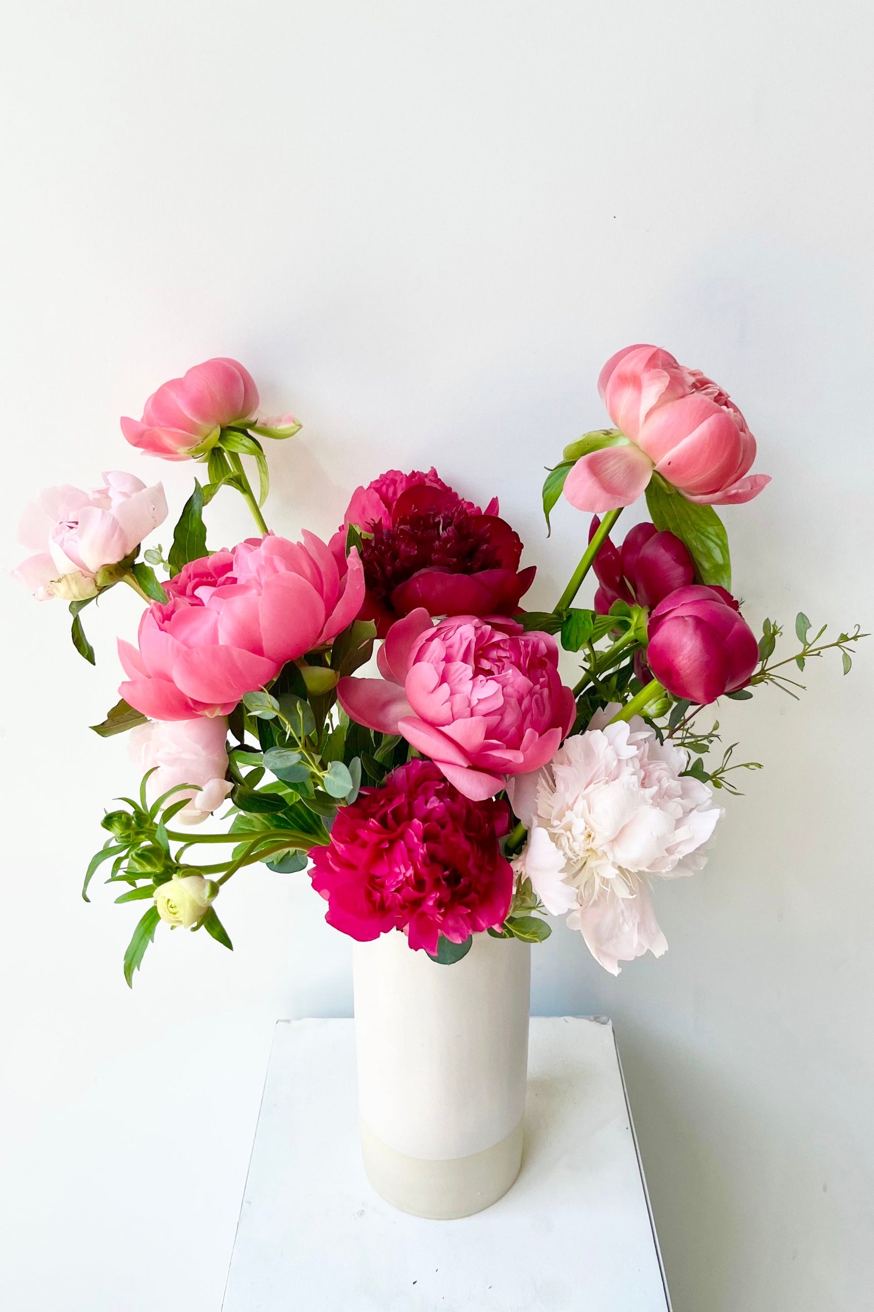 Bouquet of pink, red, and white Peony flowers in a white vase on a white surface with a white background ©Sprout Home #size_$160
