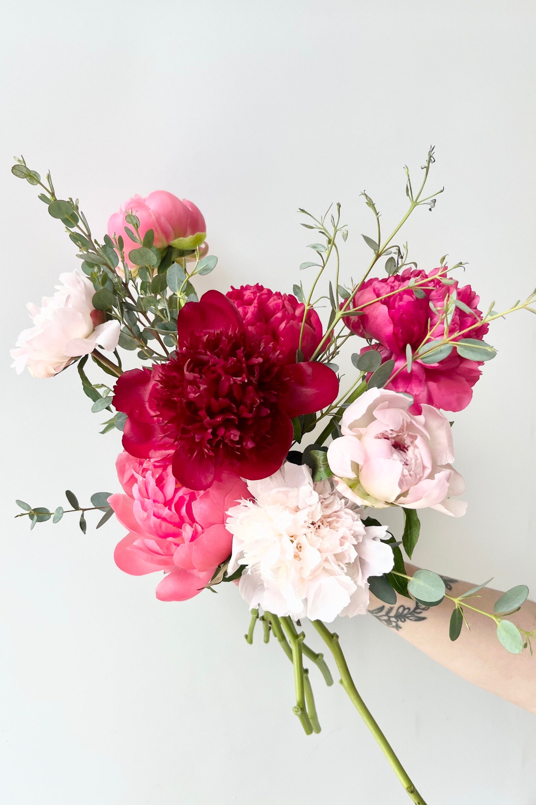 Bouquet of pink, red, and white Peony flowers on a light gray background©Sprout Home #size_$100