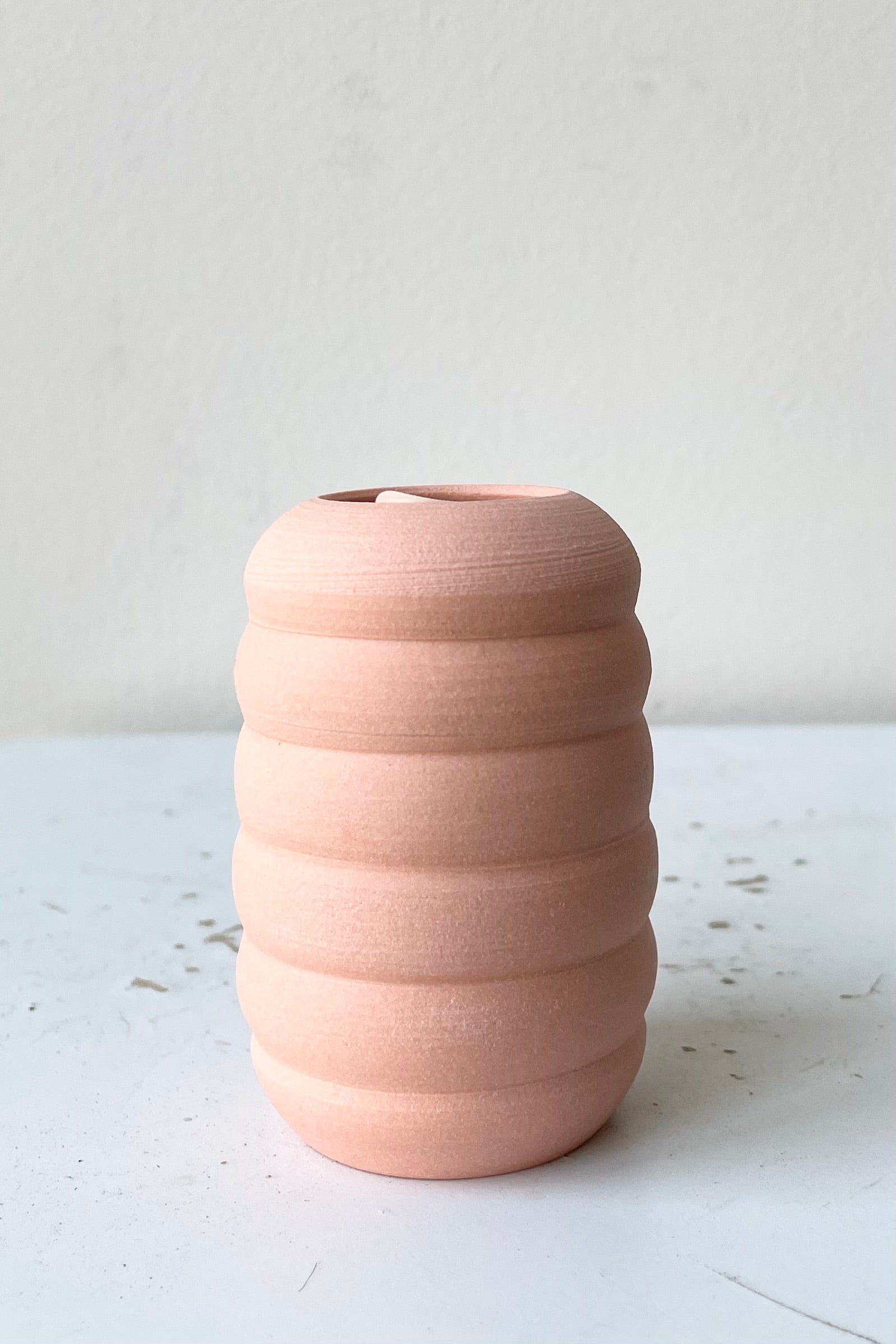 An empty petite Pastel Ribbed vase Peach in front of white.