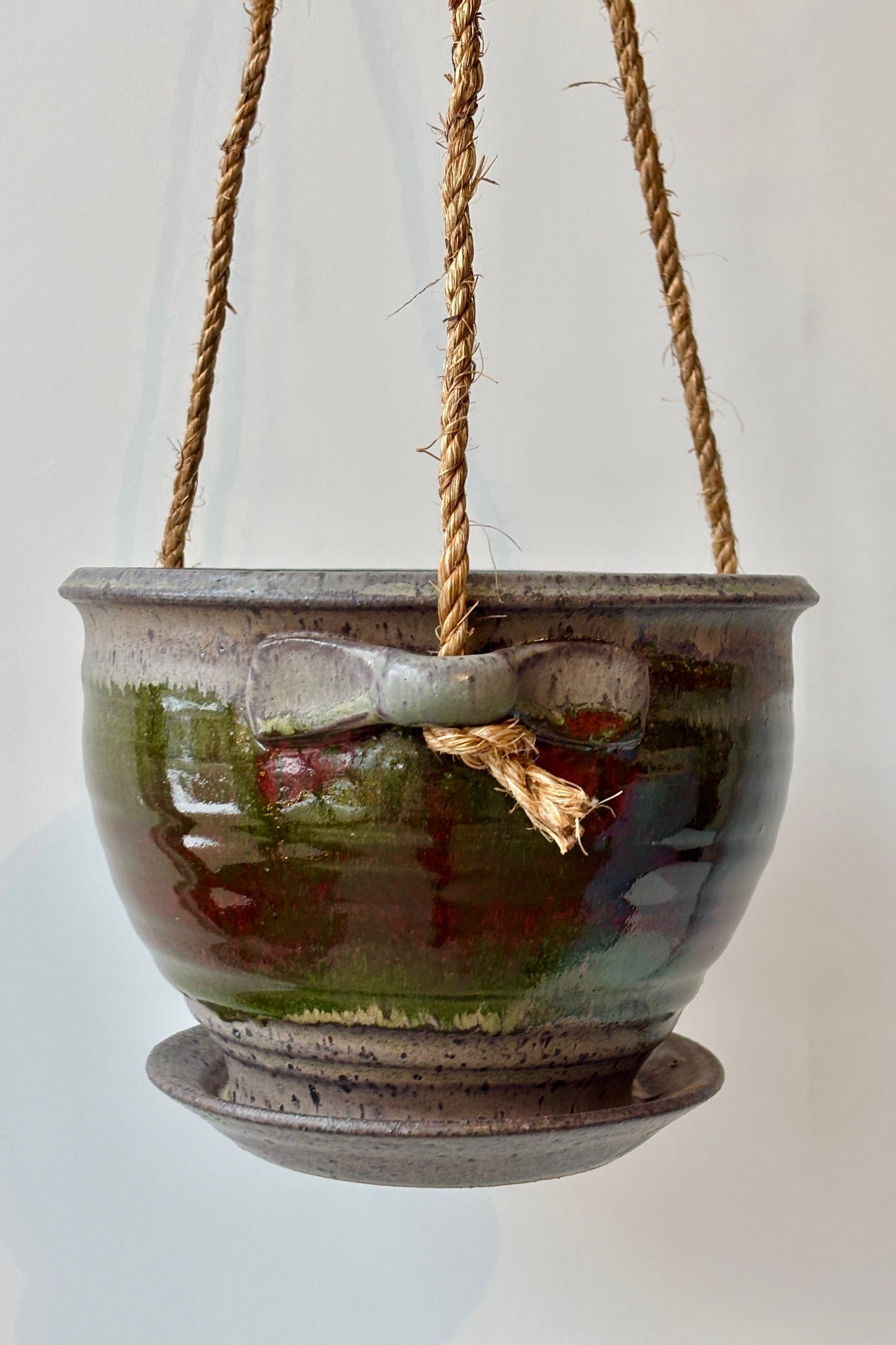 Detail of Bruning Pottery 6" diameter Hanging Planter moss & lilac glaze in various shades of green, blue, red and green held in front of white wall ©Sprout Home