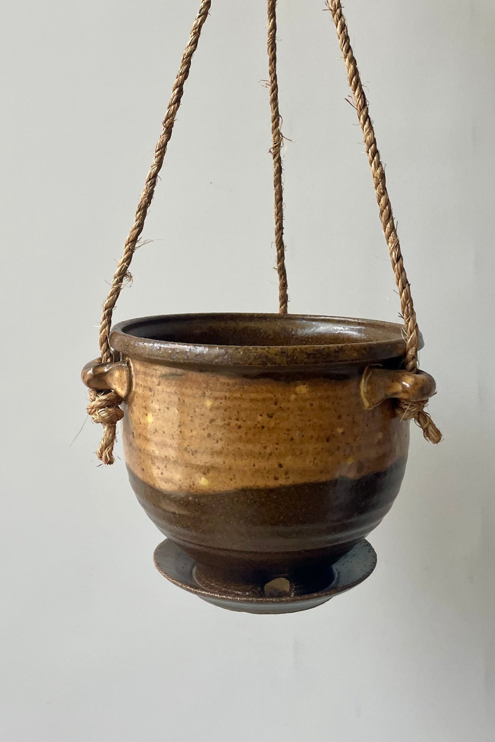 A brown and tan planter with jute cord hangs in front of a white wall ©Sprout Home