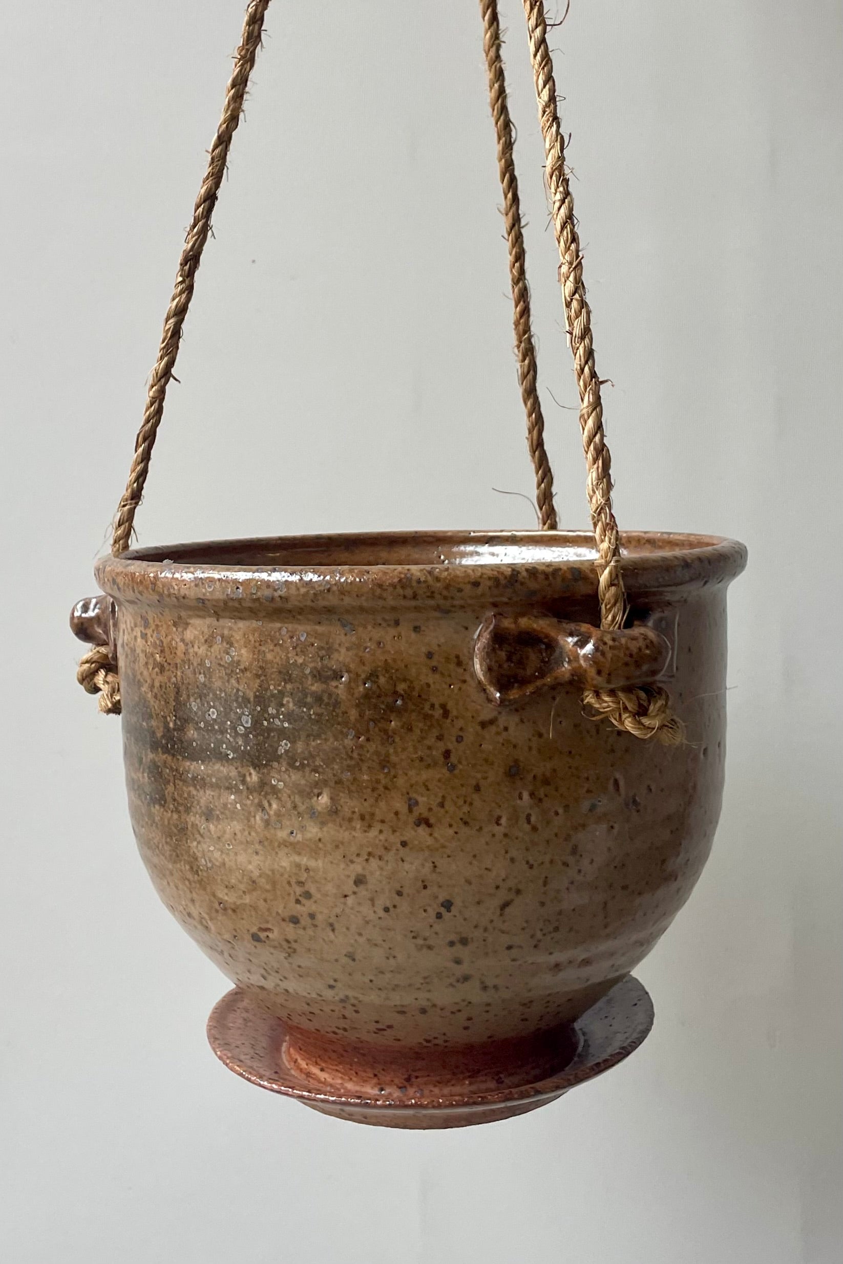 A tan speckled planter with a jute cord hangs in front of a white wall ©Sprout Home