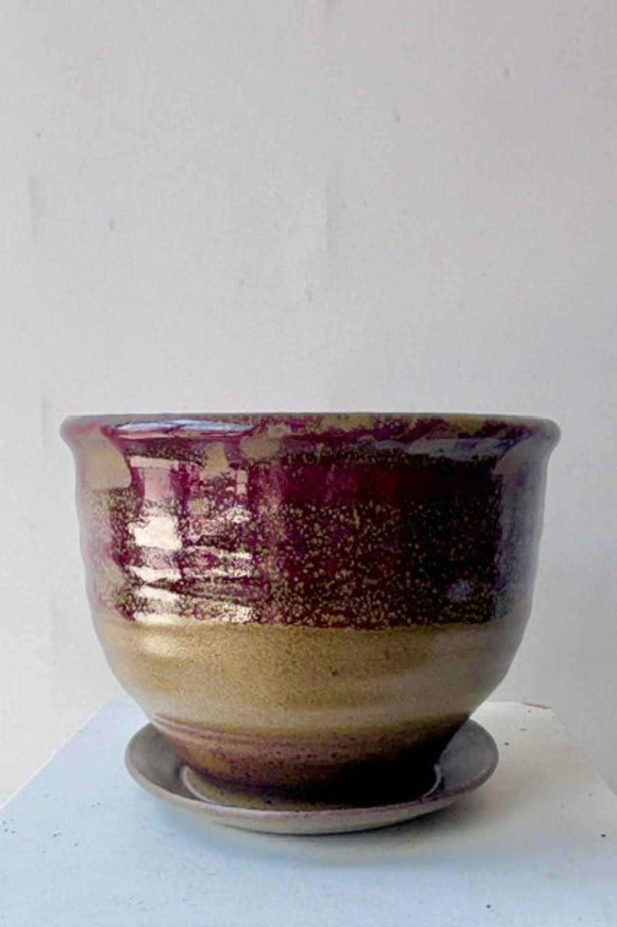 A handmade ceramic planter pot with a matching saucer, featuring a glossy glaze that transitions from a warm beige base to a deep burgundy-purple at the top, with subtle gold speckling.