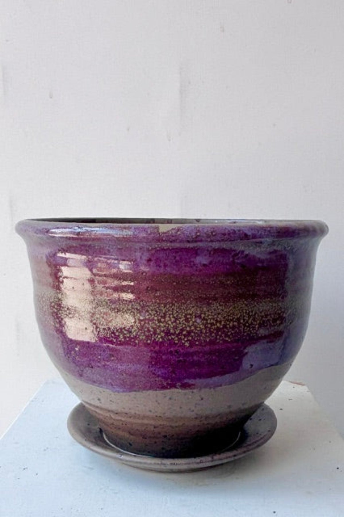 A handmade ceramic planter pot with a matching saucer, featuring a glossy glaze that transitions from deep purple at the top to a speckled brown base, set against a plain white background ©Sprout Home