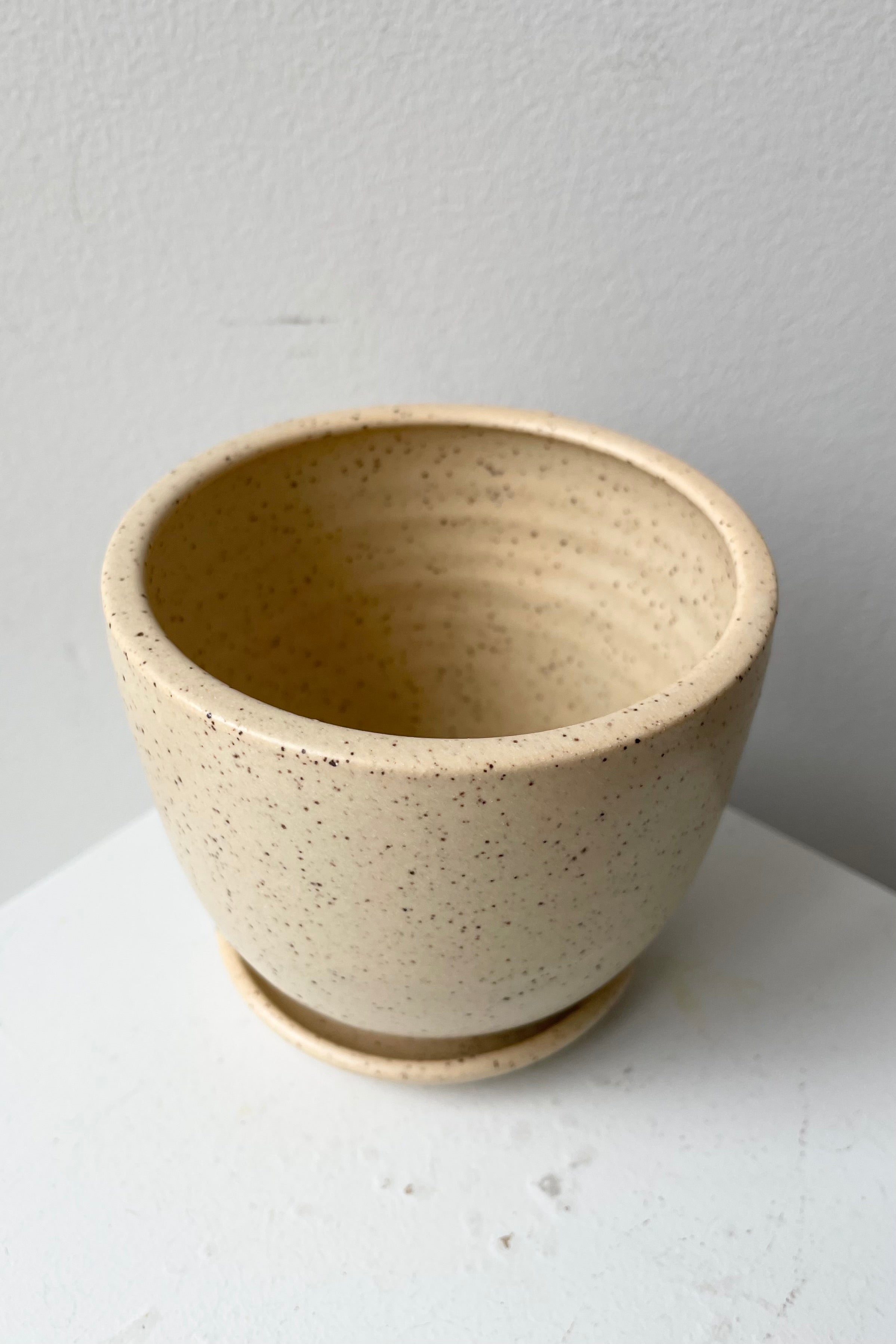 Tabletop planter and saucer in butter speckle viewed from above and side looking in.