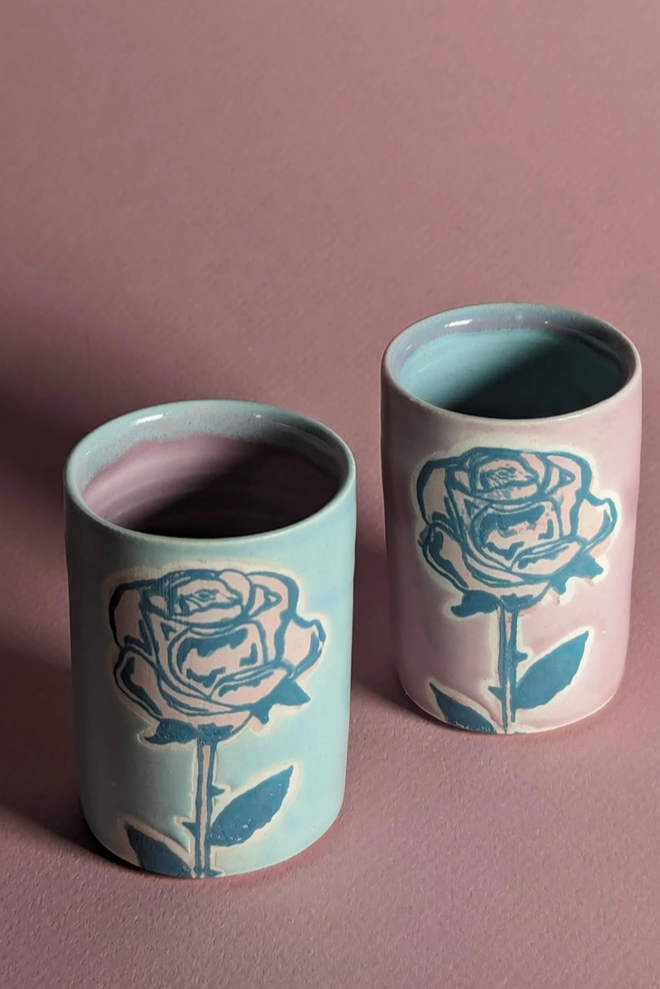 A pair of ceramic shot glasses each with a rose printed on the glaze shown on a mauve background ©City In Bloom Ceramics
