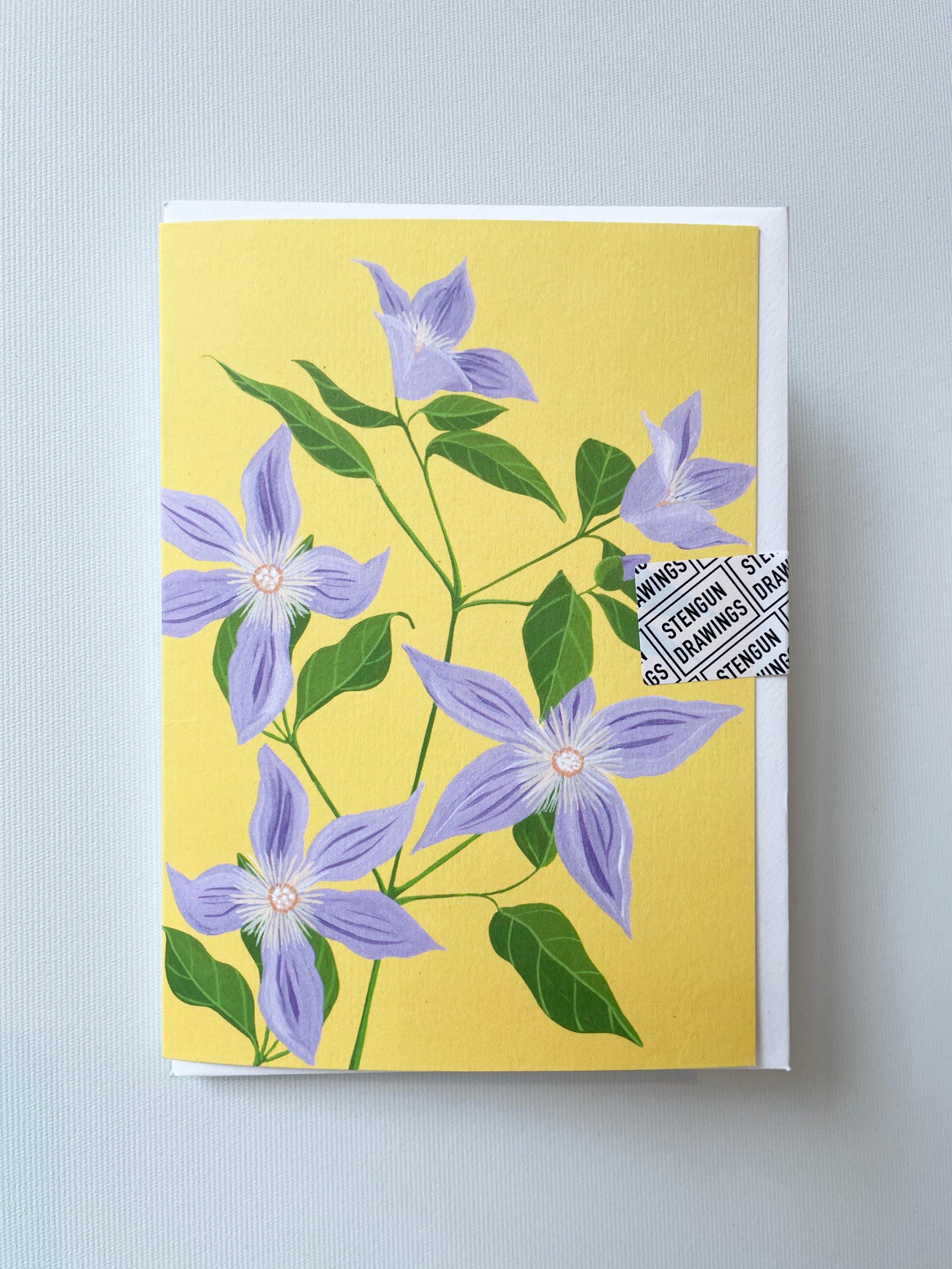 Sugar Sweet Clematis Greeting Card by Stengun shown from the front with its purple flowers and yellow background.