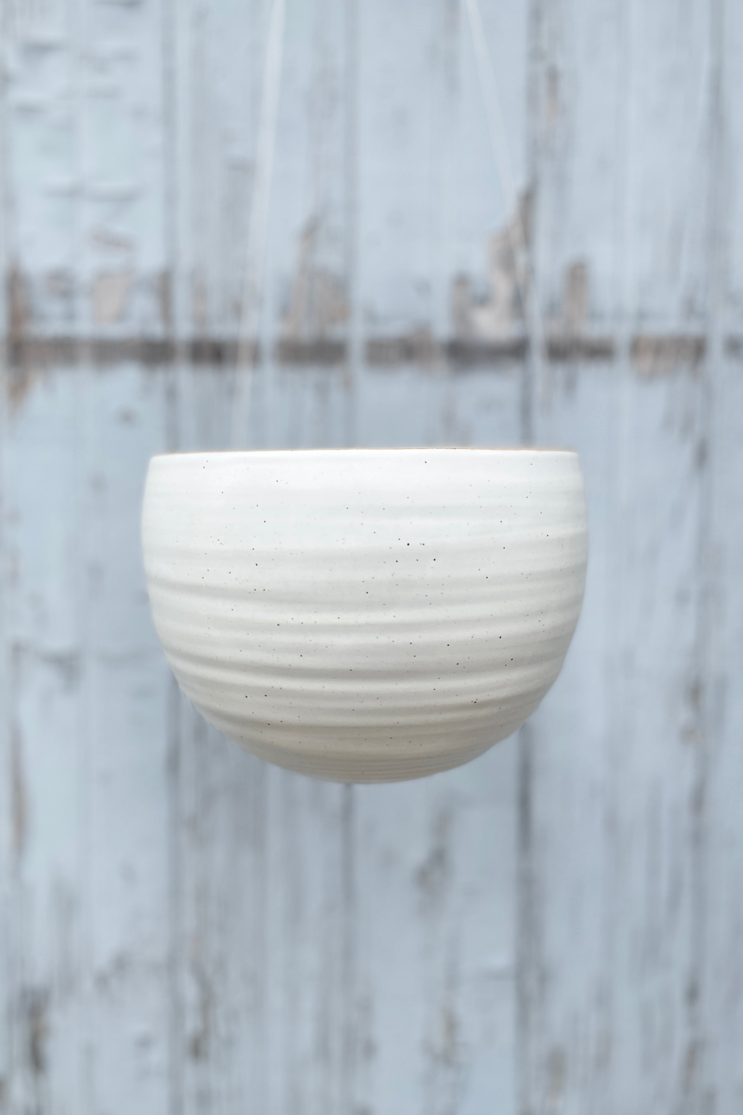 The creamy white speckle finish Spherical Hanging Planter hanging empty and viewed from the side
