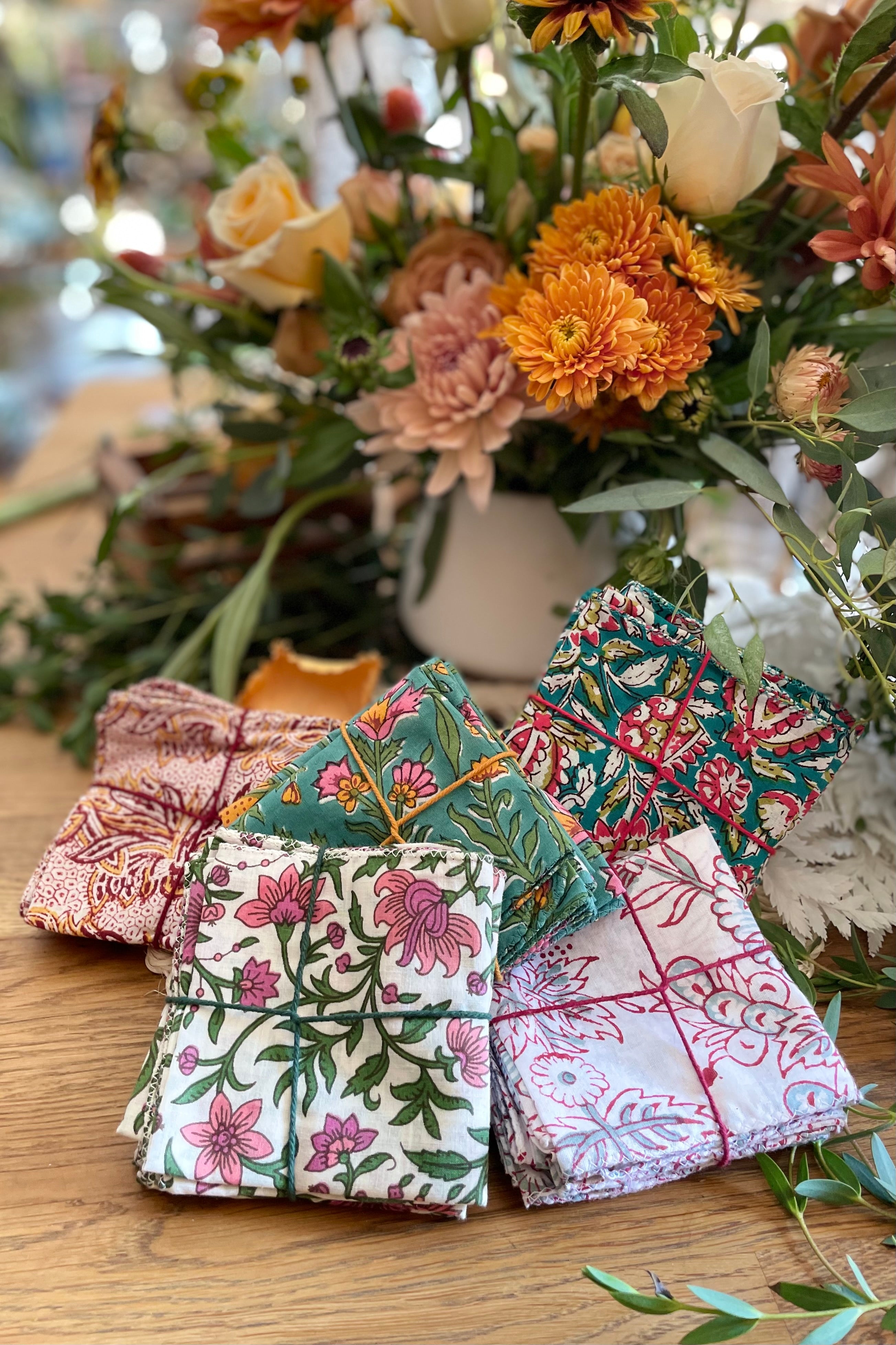 Group shot of various prints of cotton napkin sets grouped together in front of a floral arrangement.