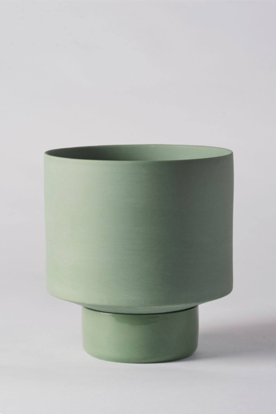 An olive green Collector's Gro pot by Angus & Celeste empty and against a white wall.