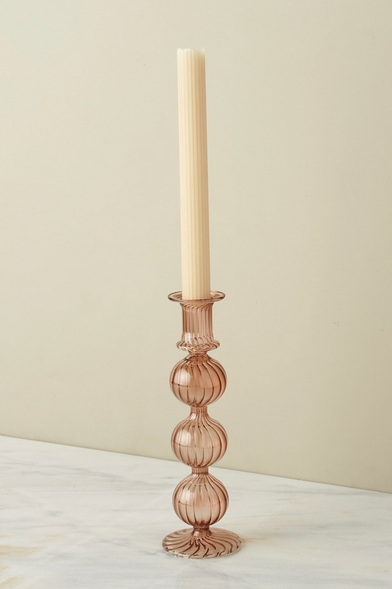 The Nahlia Candlestick in Amaranth color with a taper candle against and off white background.