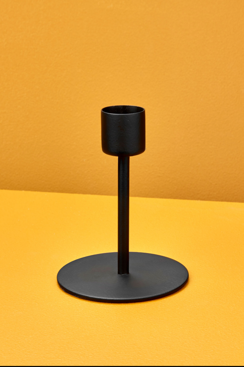 The Kent Tapered black Candlestick holder medium against a yellow wall and table.