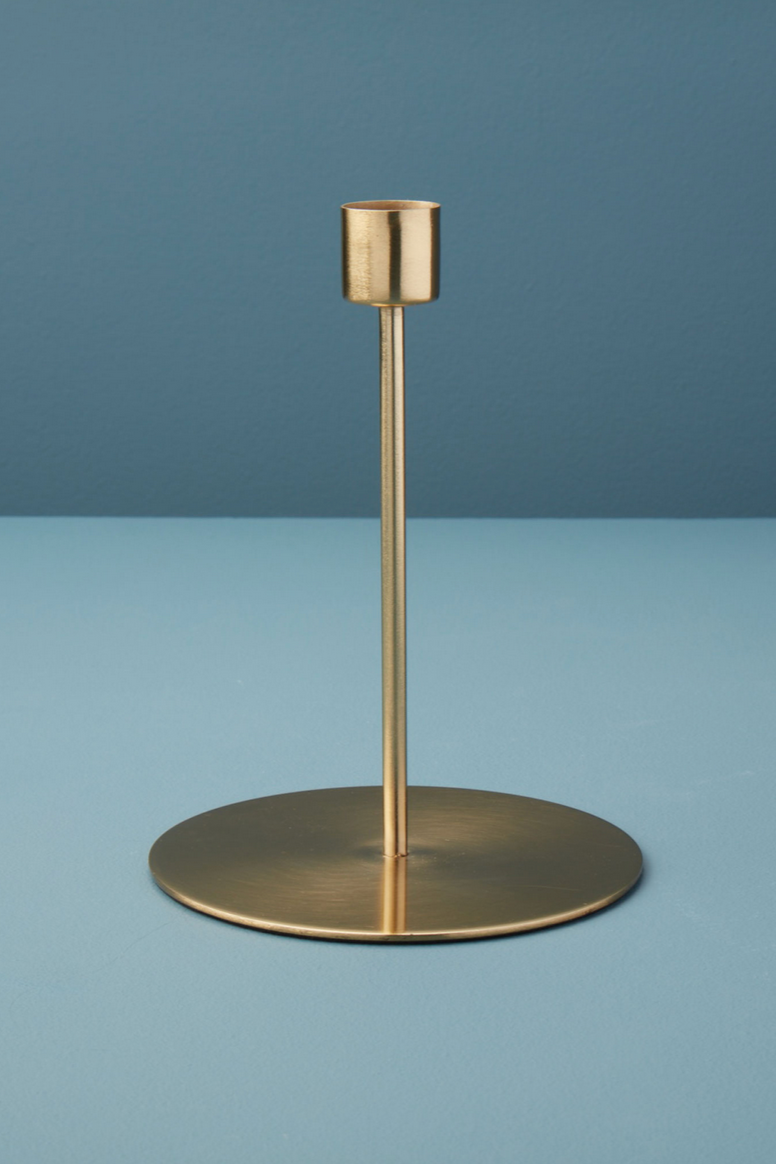 Kent gold tall candlestick holder being shown in front of a contrasting blue.