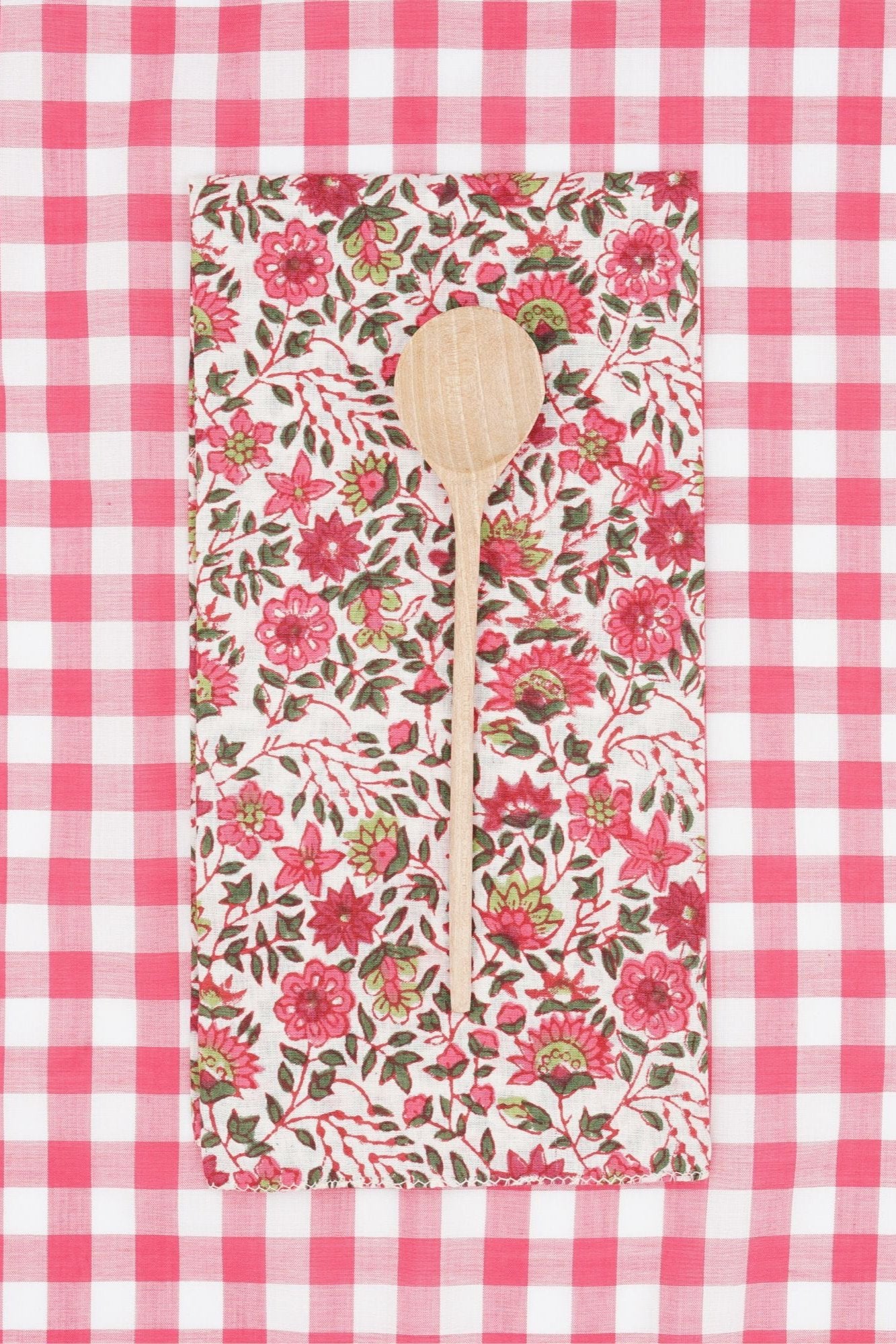 Cotton Napkin Chicorée Peonie folded in to a rectangle, wood spoon on top and a red and white checkered backdrop.