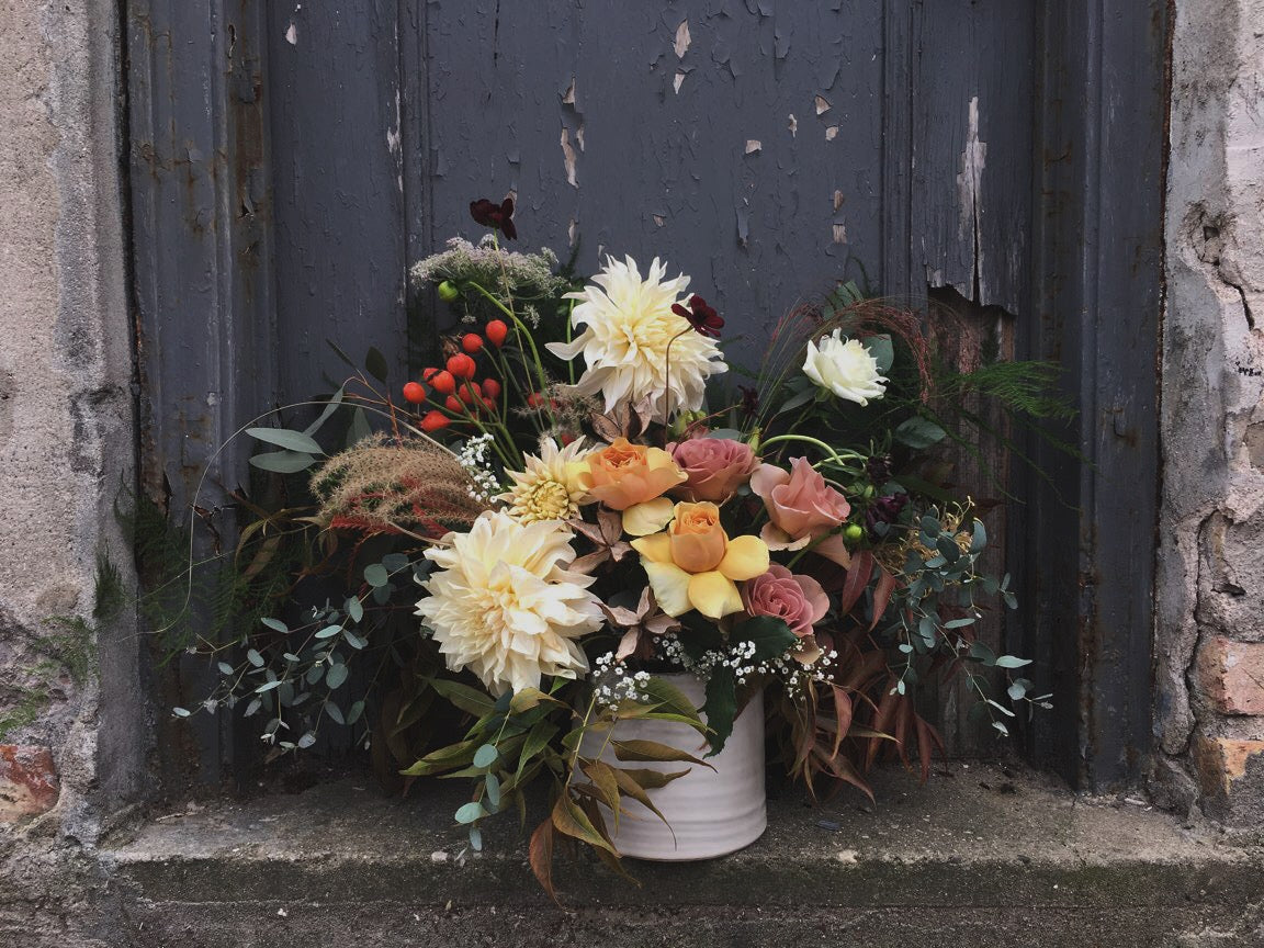 A soft and inviting fall arrangement by SPROUT HOME featuring fluffy white dahlia in front of a gray door. Photo by Sprout Home.