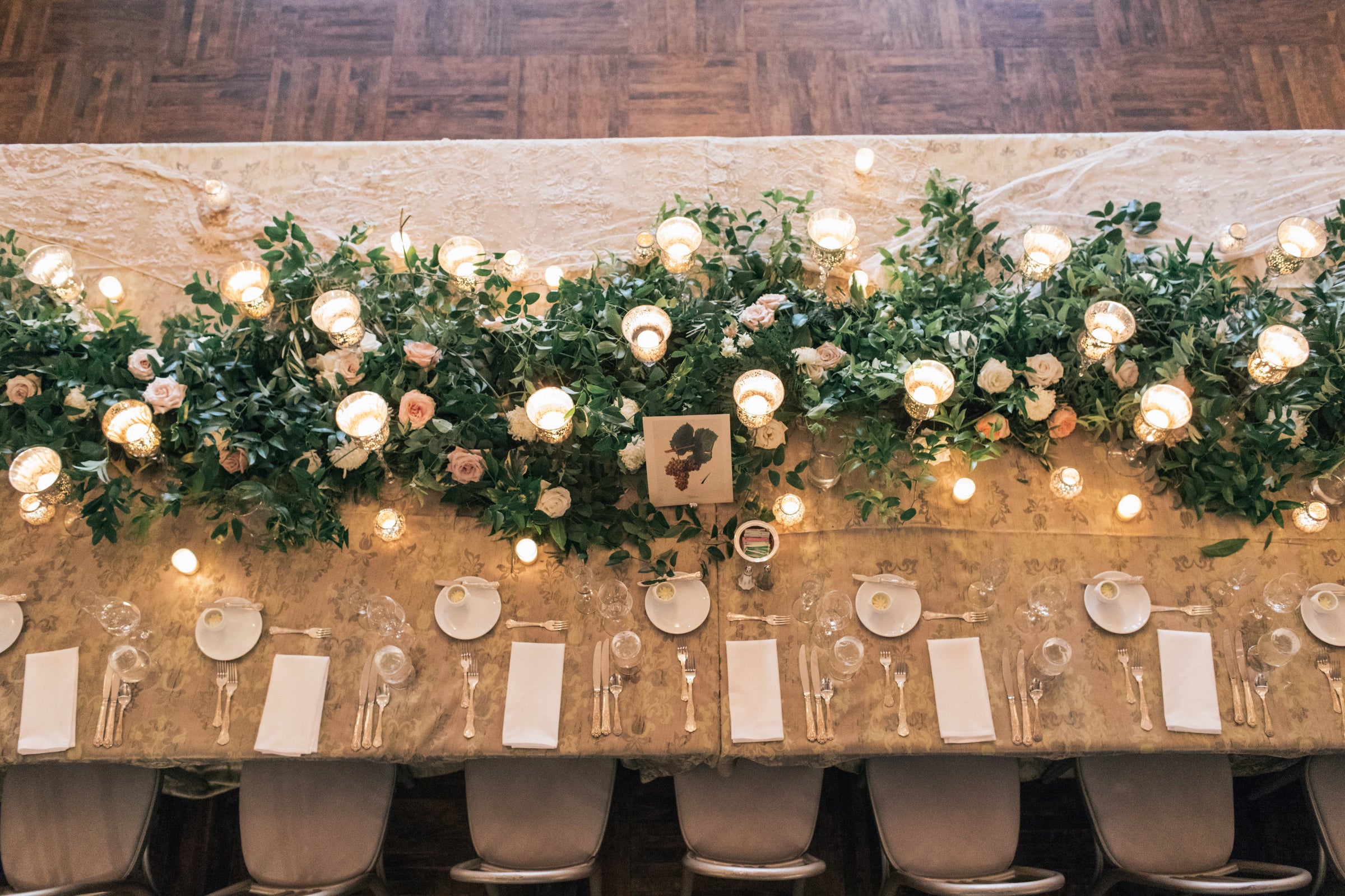 green wedding garland with white and pink floral and candles stretching down a table from above. Photograph by Shannon Olesiak Photo