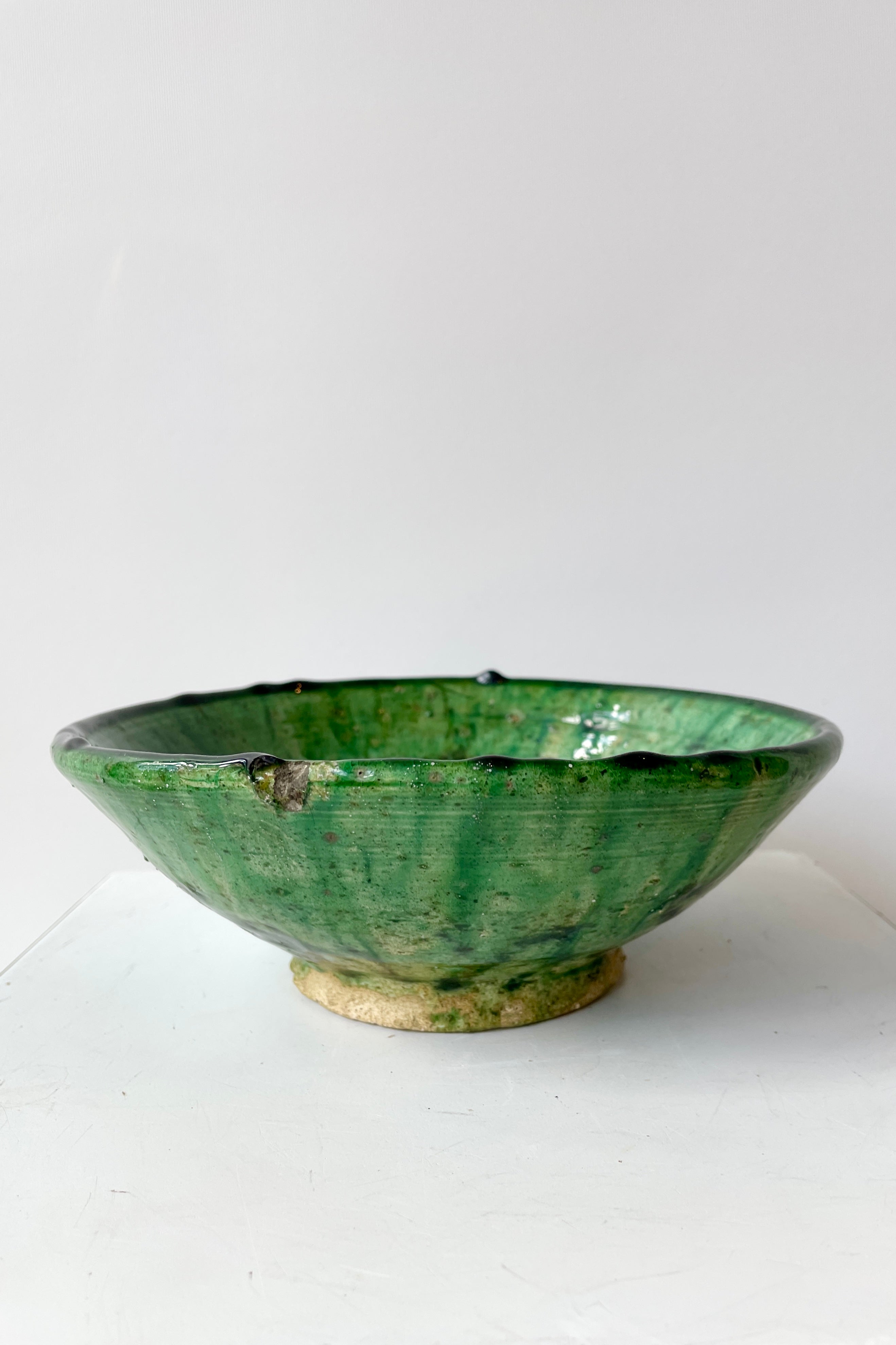 The Tamegroute green bowl in small looking at it from the side against a white wall.