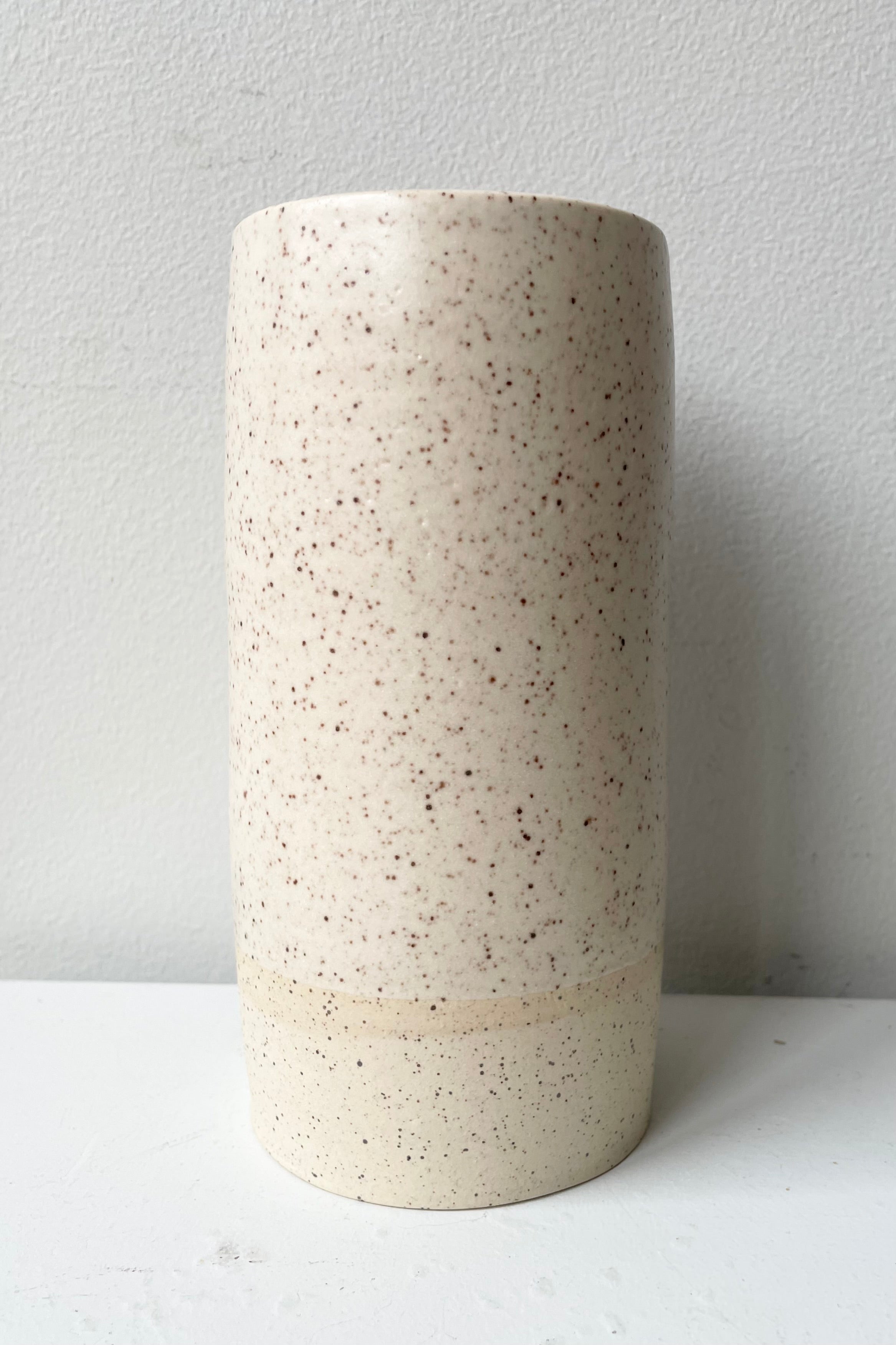 Cream Speckle Jacqueline vase Small against a white wall.