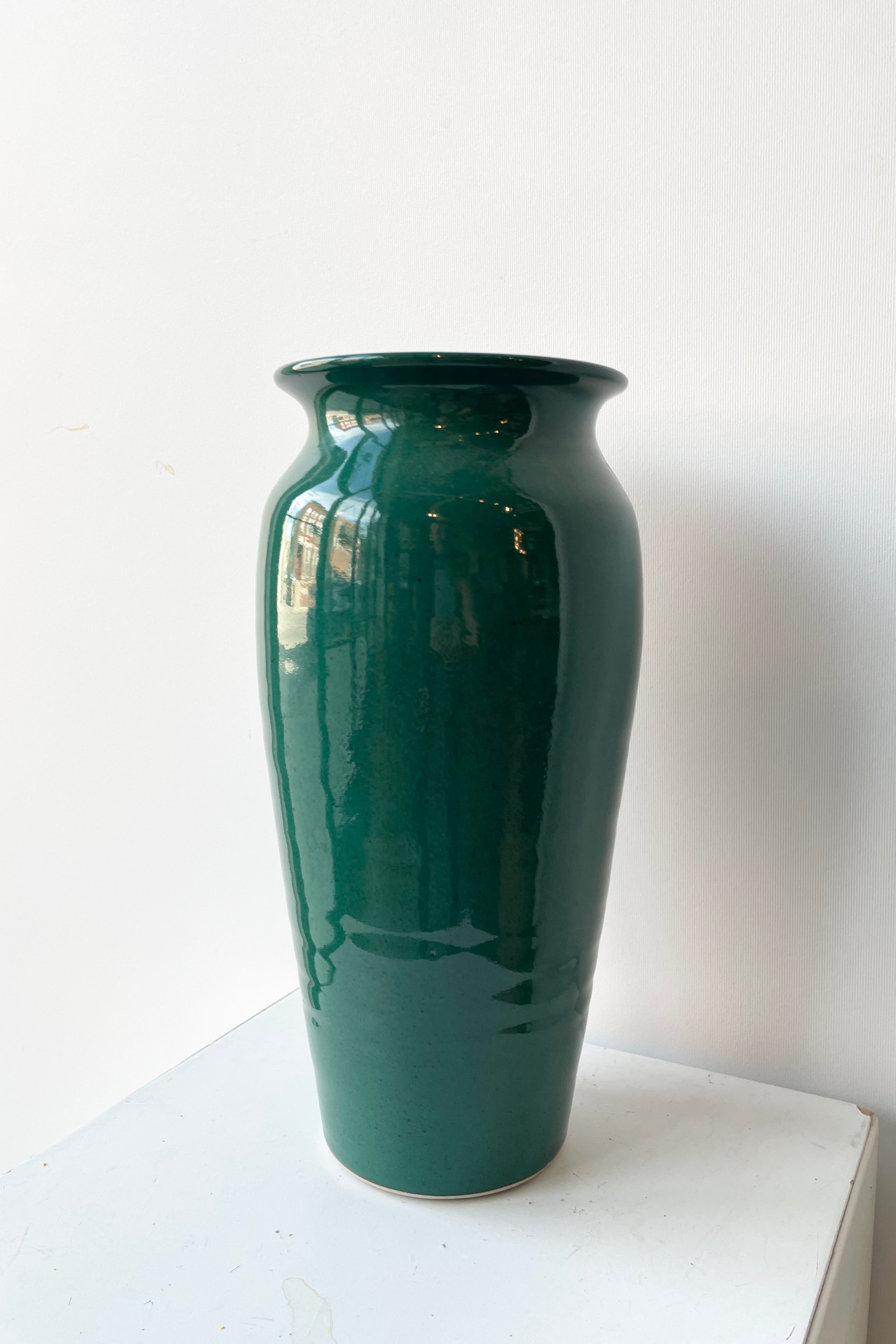 The Tall vase in jade green glaze viewed from the side against a white wall.