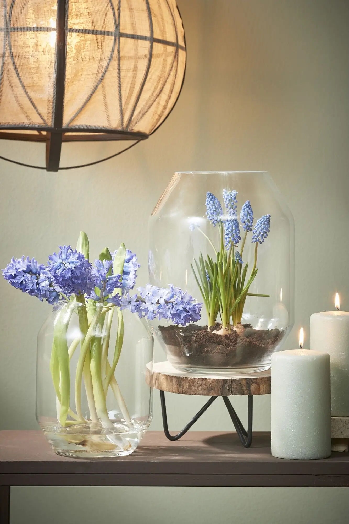 Decorative setup with flowers in Dali glass vases and a candle on a wooden surface. ©Creation Jute USA