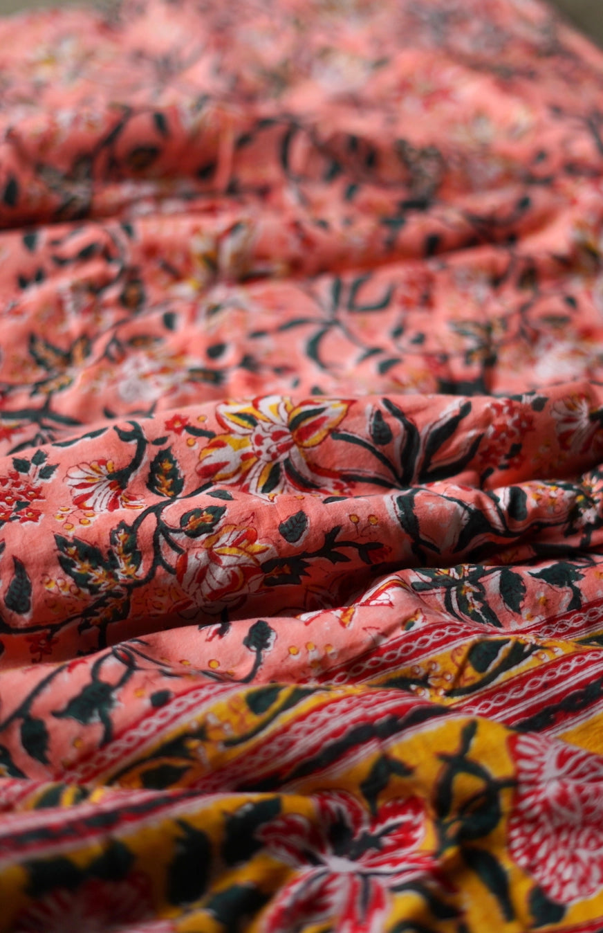 Close-up of a folded fabric on a reversible blanket with floral patterns in pink, black, and yellow. ©Annahmol