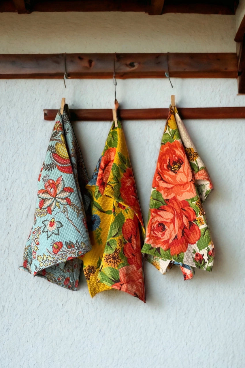 Three floral towels hanging on a wooden rack against a white wall. ©Annahmol