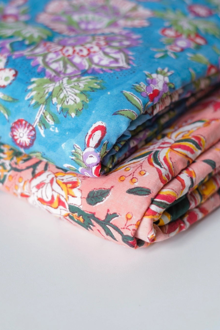 Stack of Block Print Reversible Summer Cotton Blanket colorful folded fabrics with floral patterns on a light background ©Annahmol