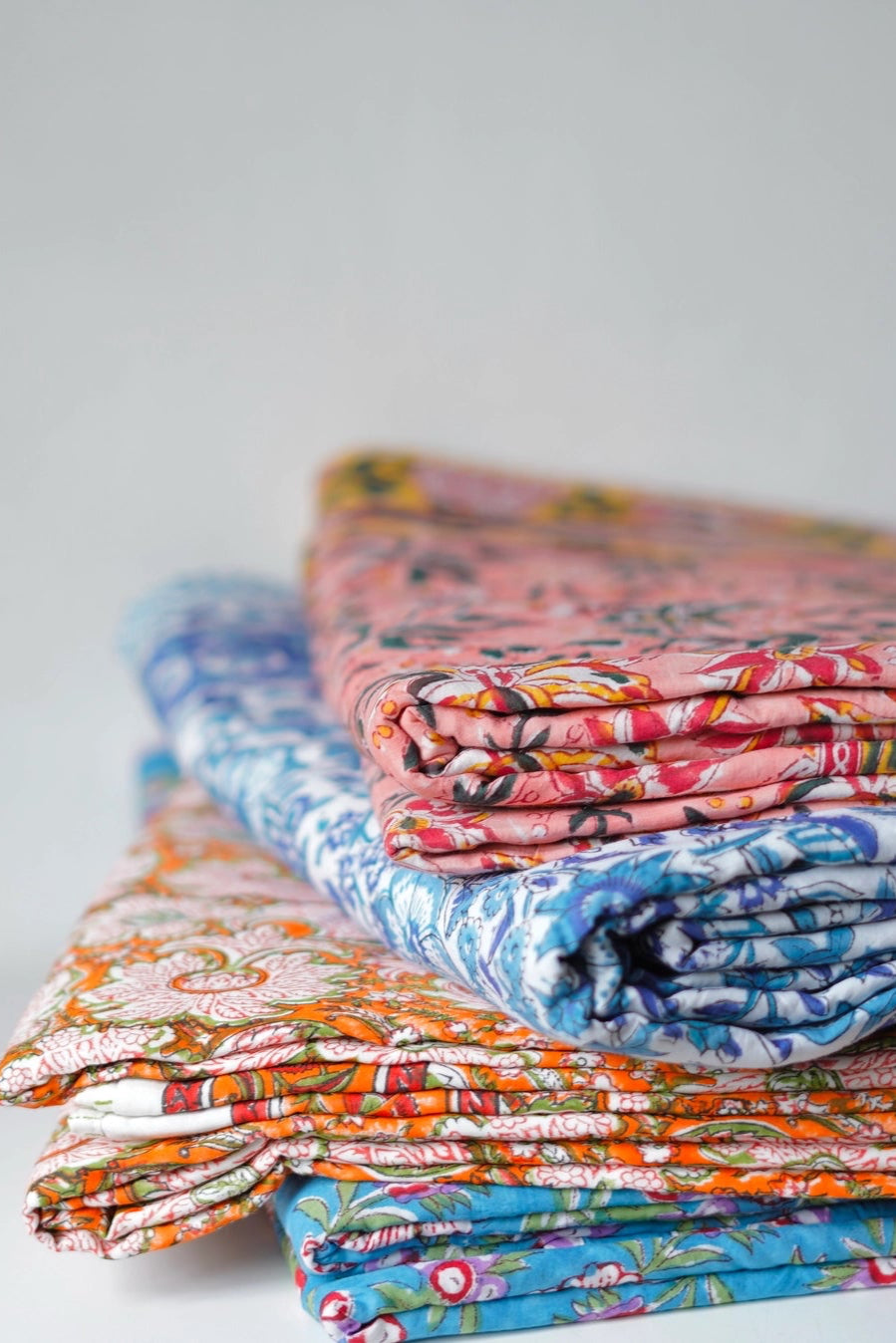 Stack of Block Print Reversible Summer Cotton Blanket colorful folded fabrics with floral patterns on a light background ©Annahmol