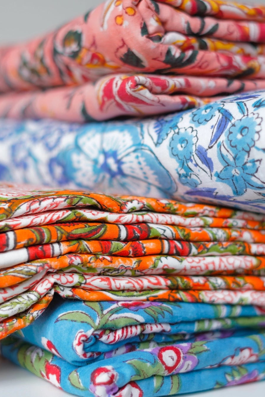 Stack of Block Print Reversible Summer Cotton Blanket colorful folded fabrics with floral patterns on a light background ©Annahmol